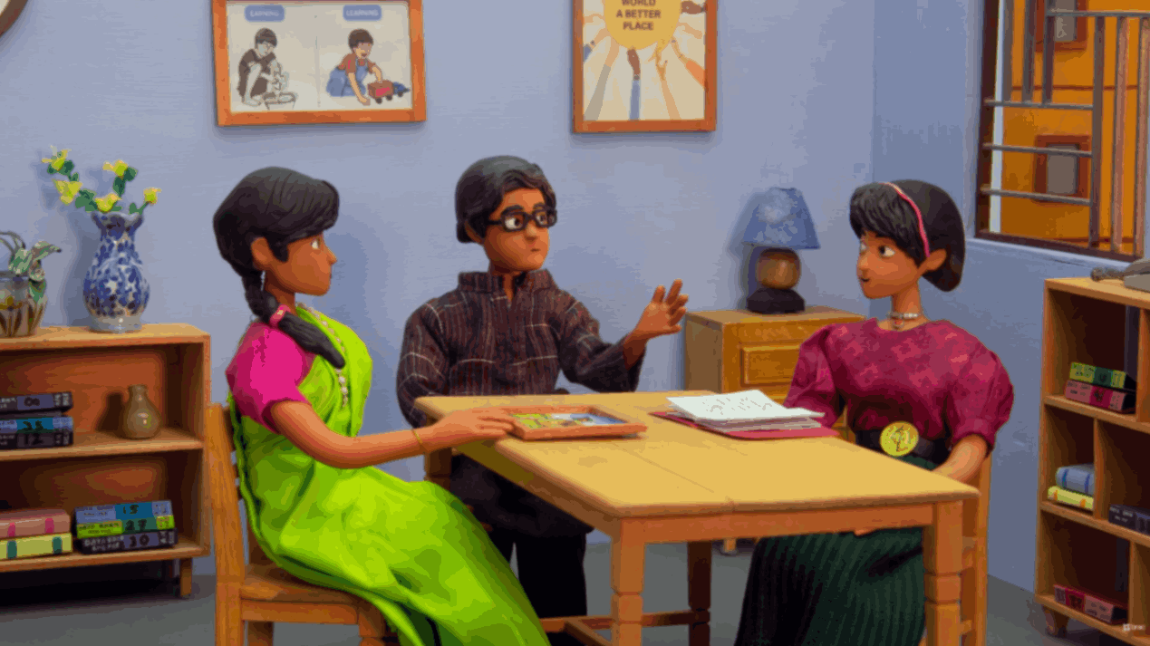 Two women and a man sitting at a table discussing school materials and books.