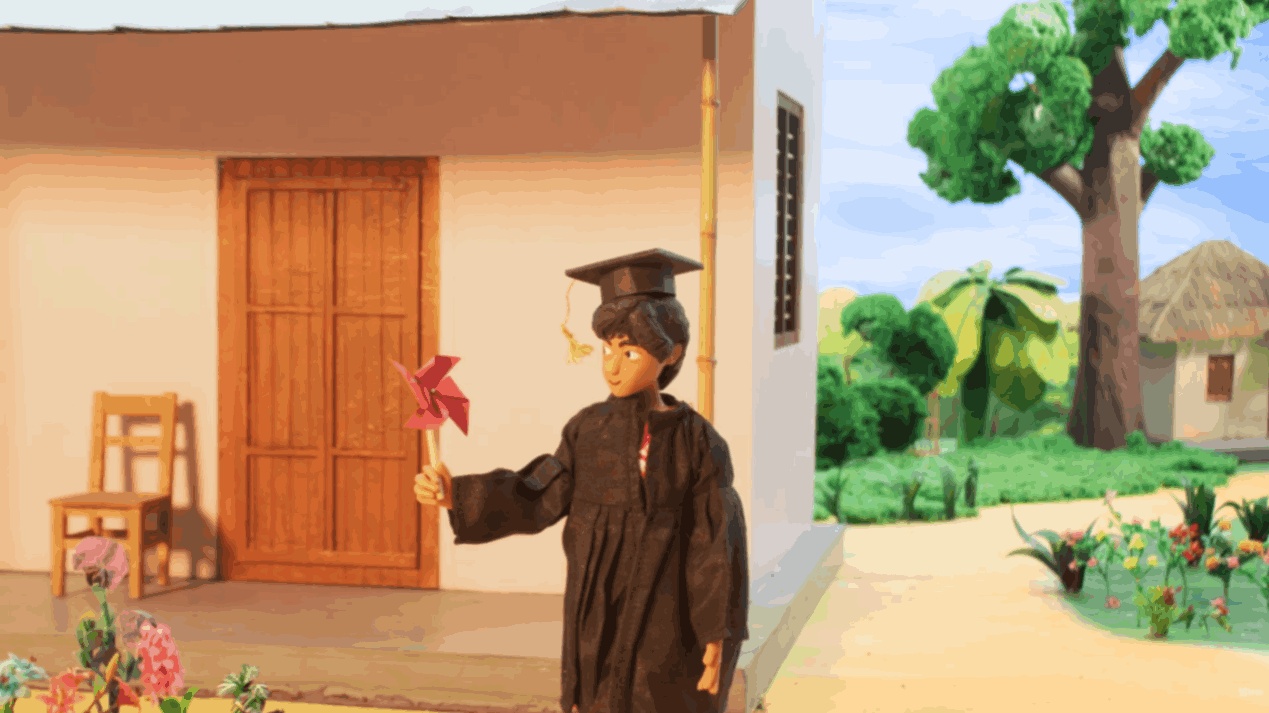 Child wearing a graduation cap and holding a red pinwheel outside a village home.