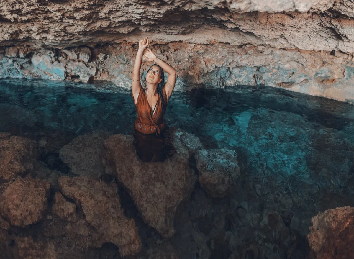A girl wearing a red dress poses for a photo inside Cenote Aldea Zama in Tulum.