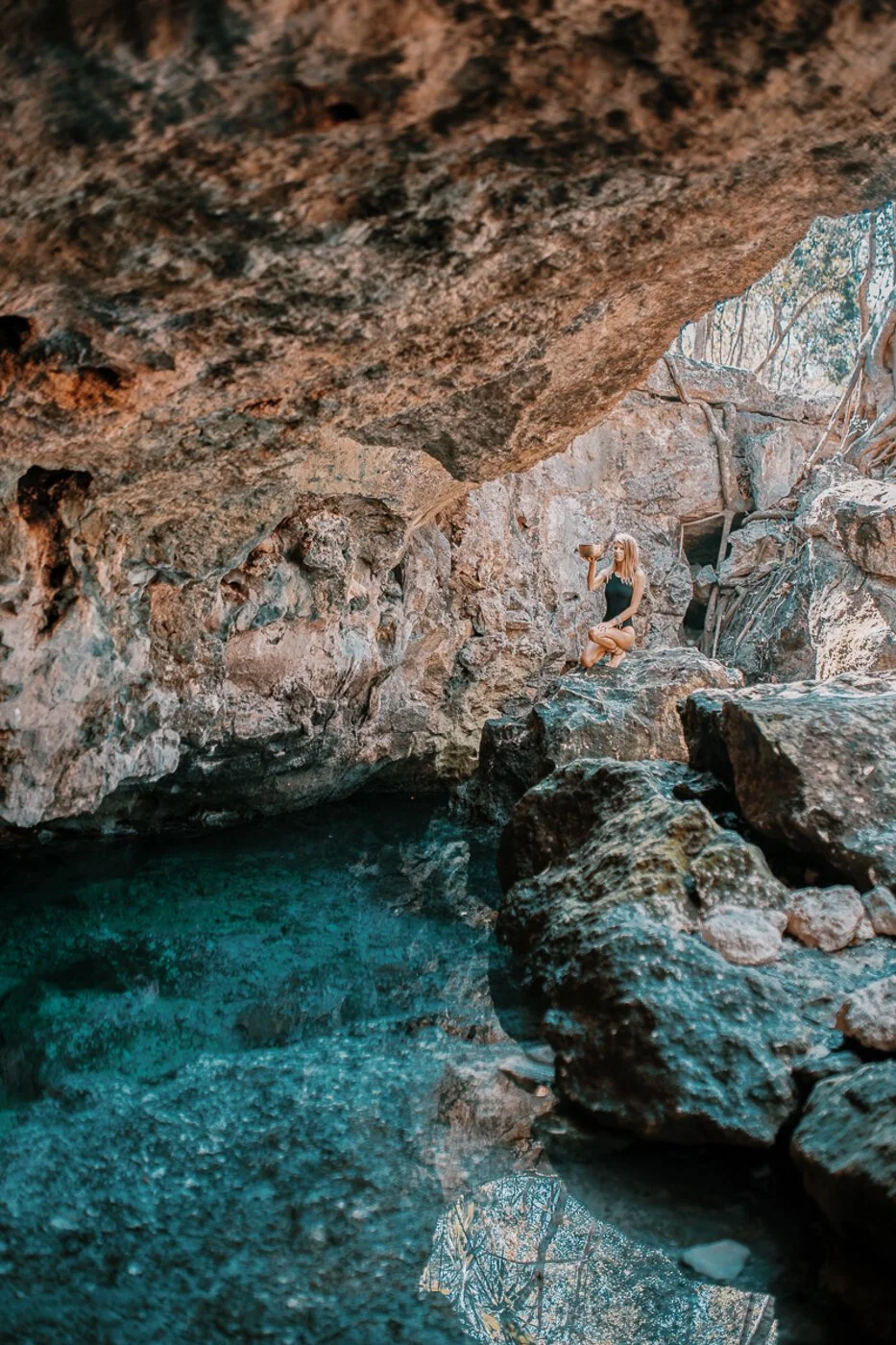 A girl poses on a rock at the bank of the water at Cenote Aldea Zama in Tulum, Mexico. 