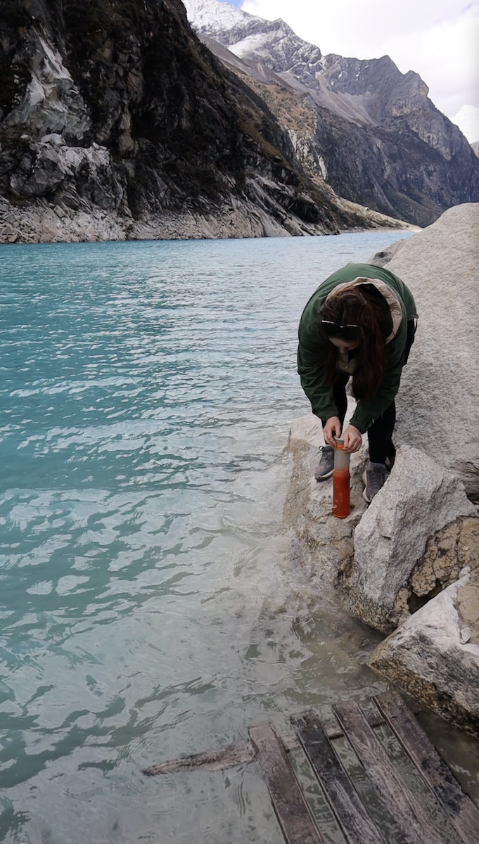 Blogger Katie Caf uses her GRAYL travel water purifying bottle to drink water out of a glacier lake in Peru. 