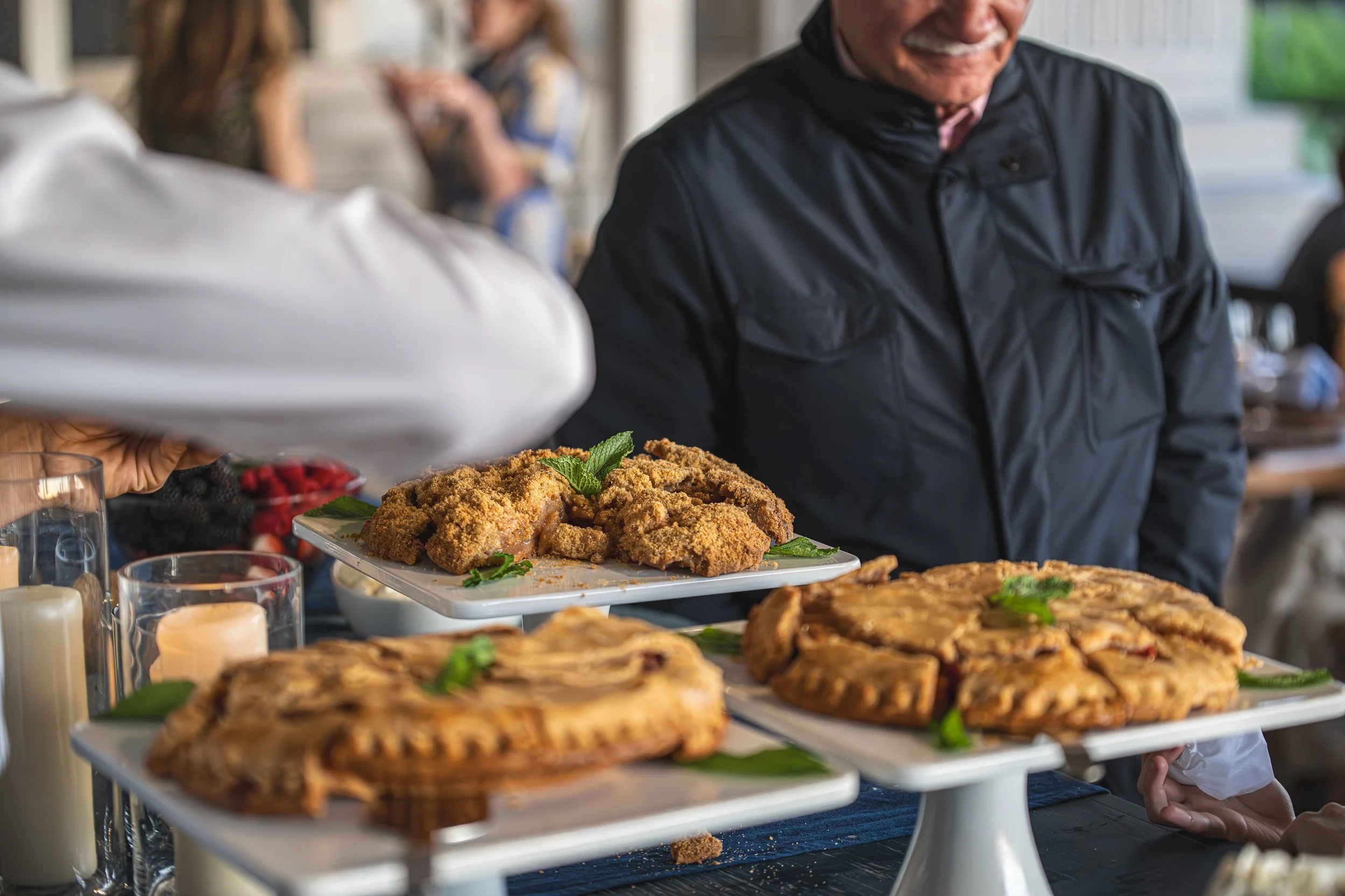 Person holding a platter of fried chicken garnished with mint at a buffet table with various dishes.