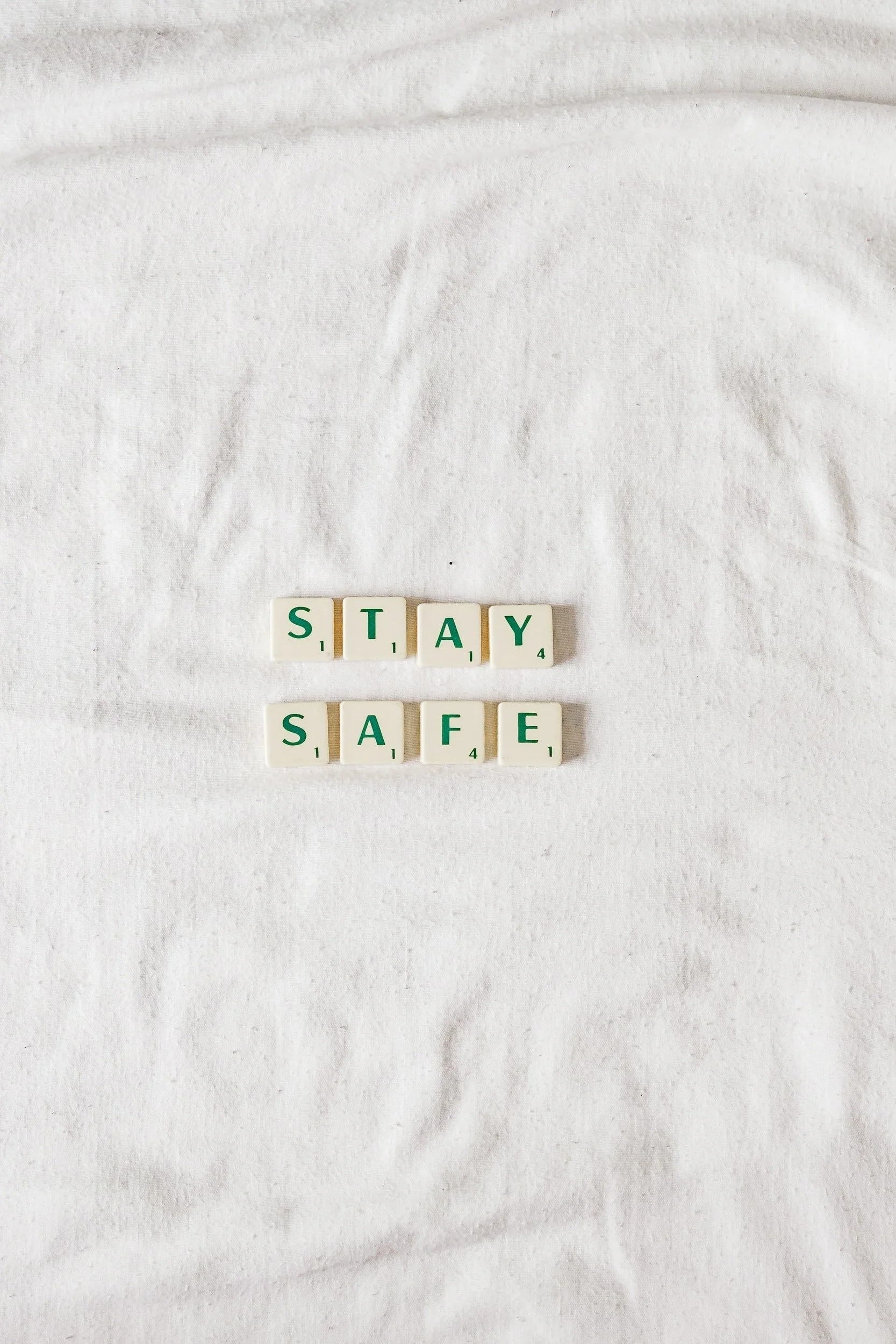 Scrabble tiles on white fabric spelling out the words "stay safe".