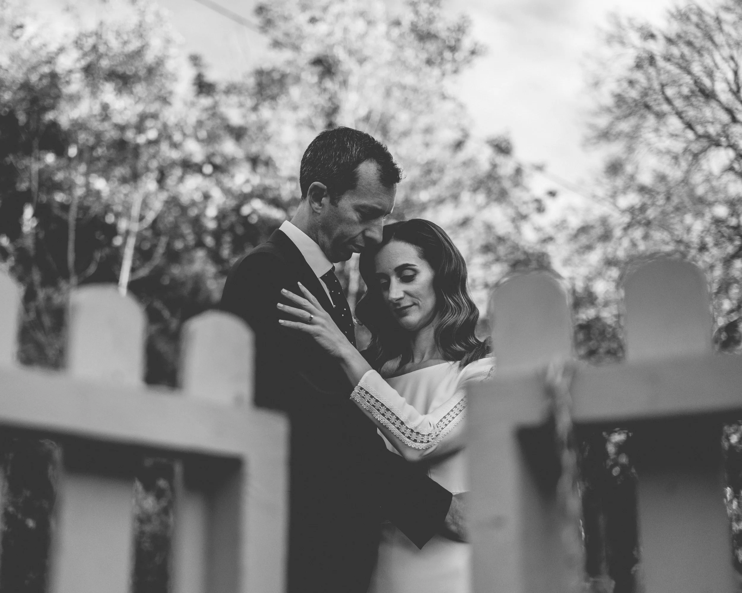 A couple dancing closely outdoors on a sunny day with trees in the background.