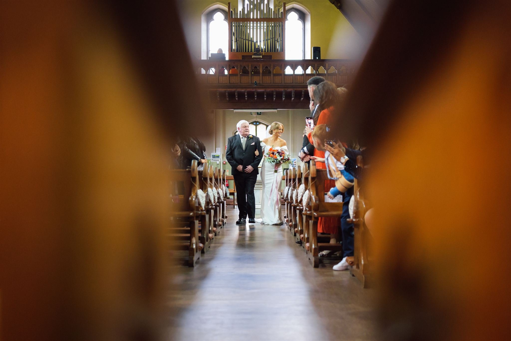 A bride walking down the aisle, being escorted by an older man, in a church decorated for a wedding.