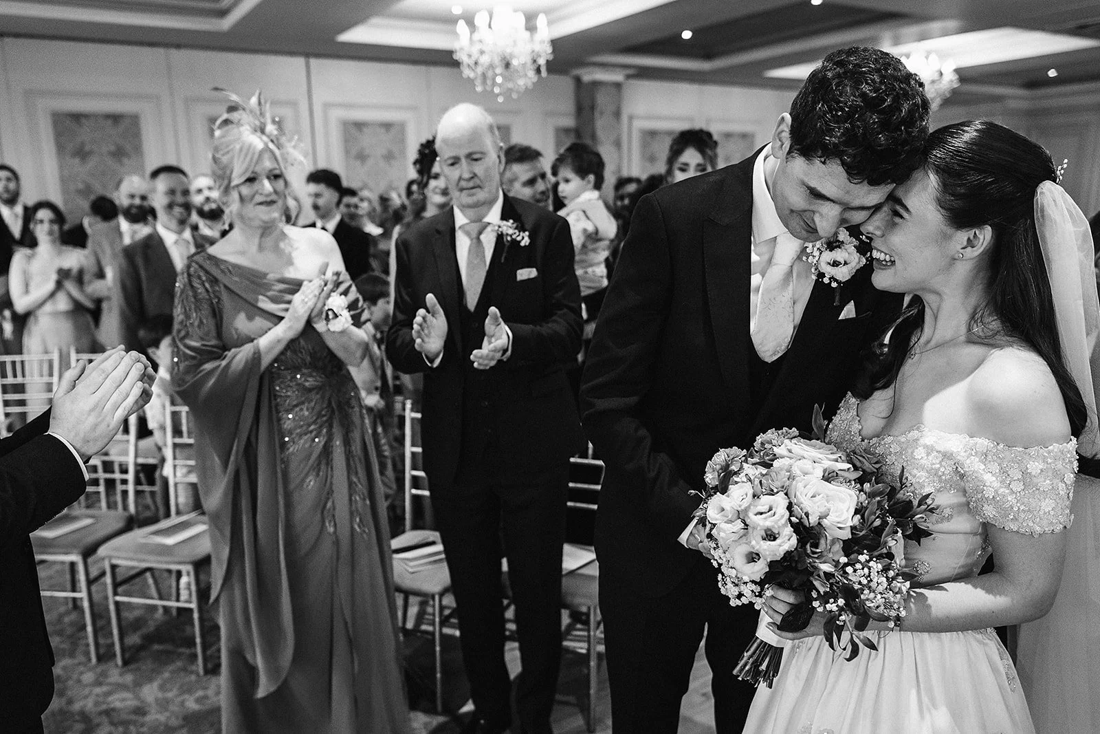 A wedding ceremony with a bride and groom sharing an intimate moment, surrounded by guests in an elegant indoor setting.