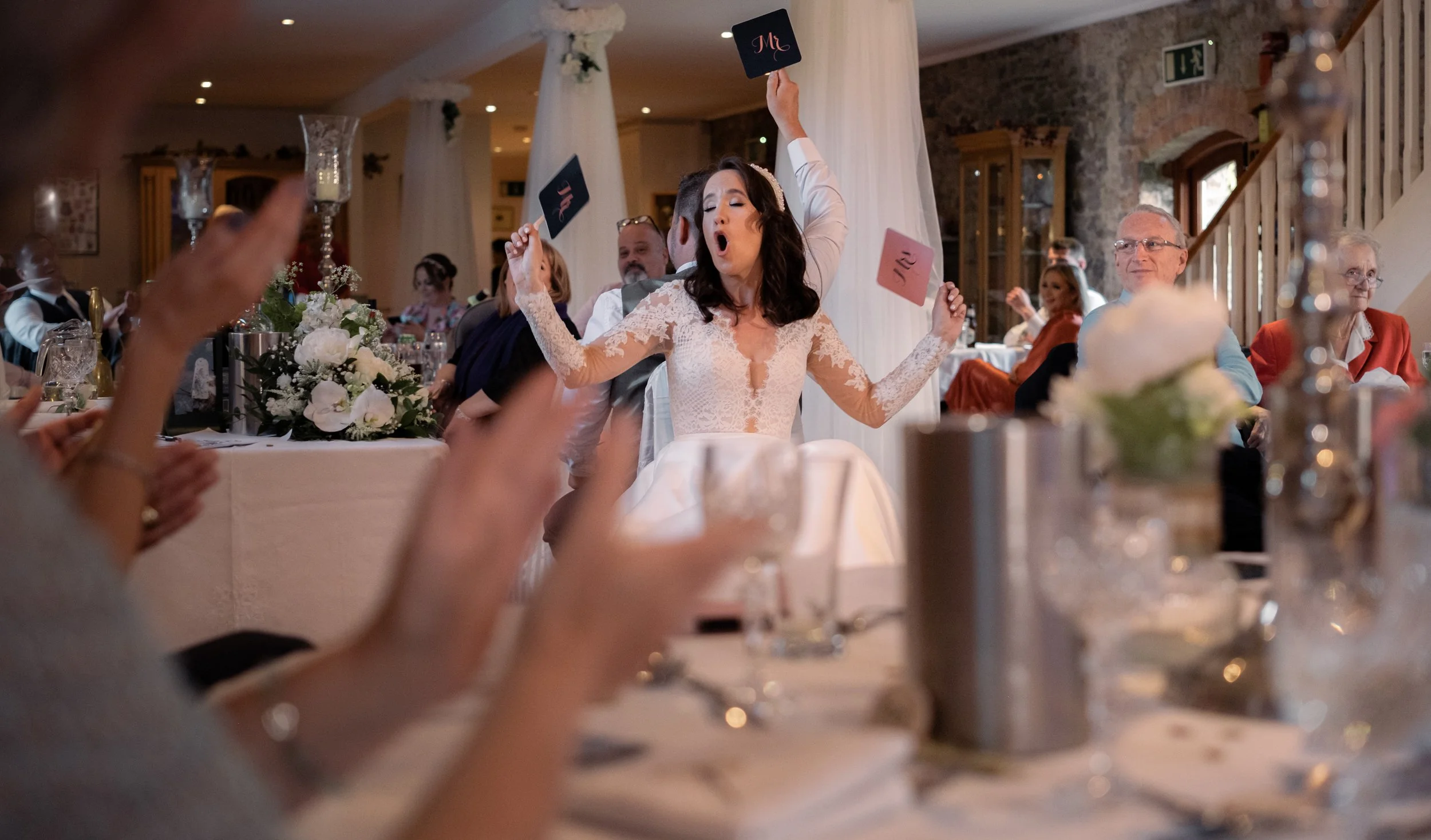 Bride dancing at her wedding reception, surrounded by seated guests, with floral centerpieces and candles on the table.