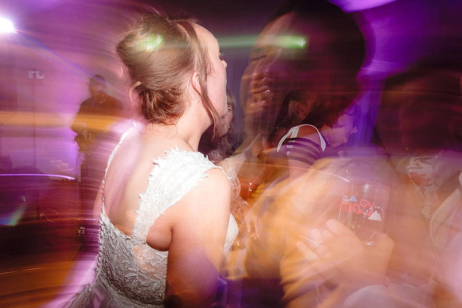 A woman in a white lace dress dancing at a party with colorful lights and other people in the background