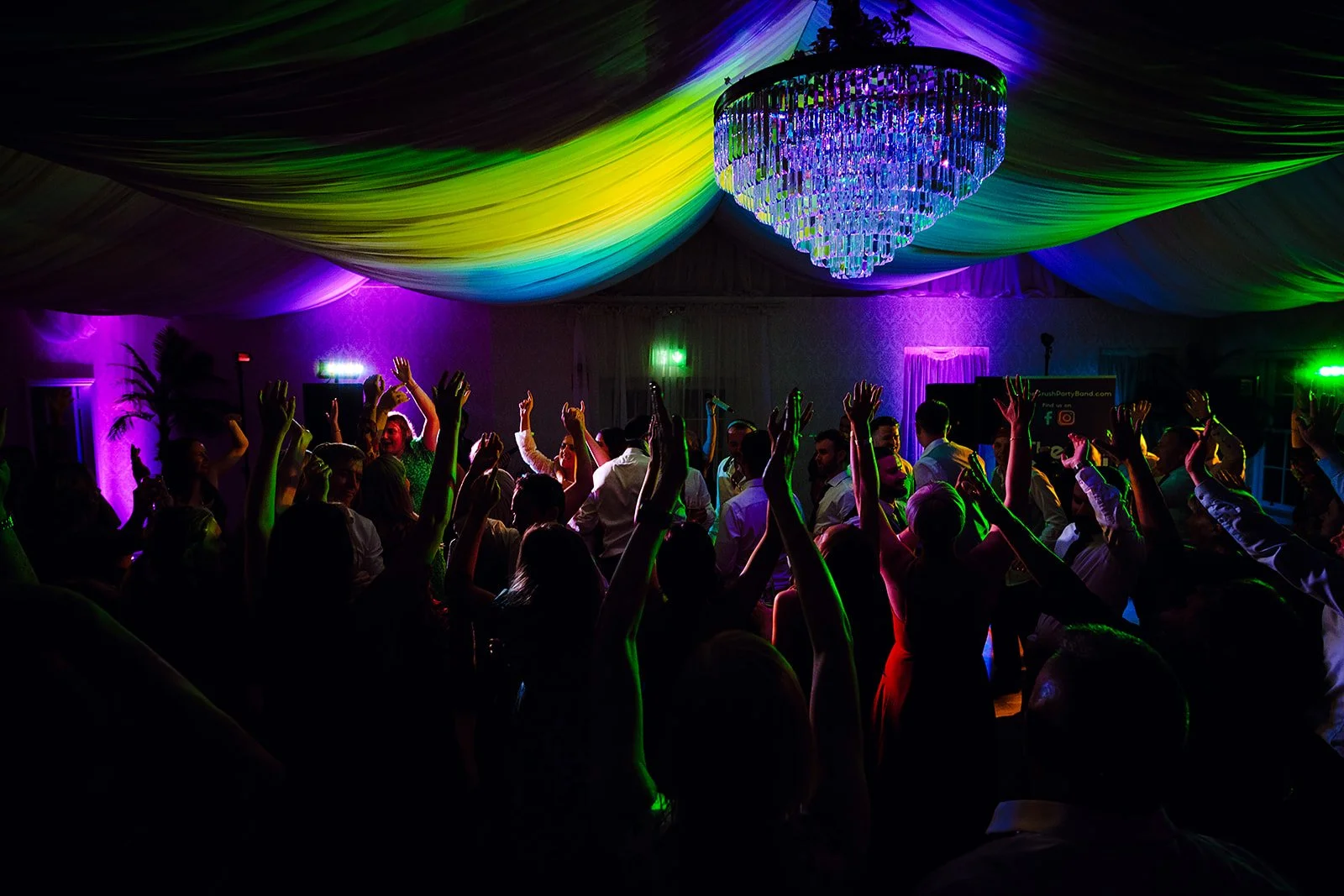 People dancing at a party with colorful lighting and a large chandelier hanging from a decorated ceiling.