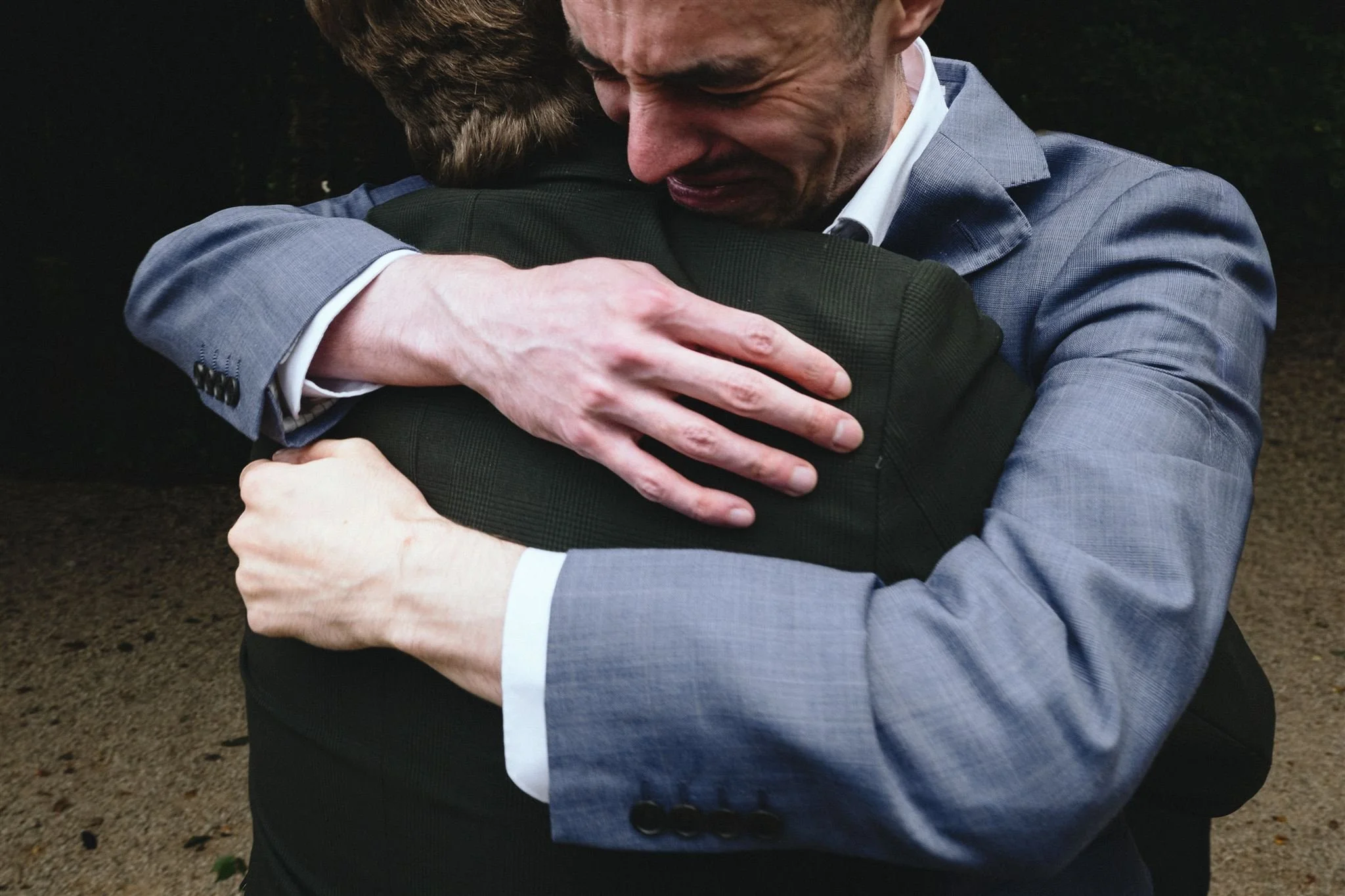 Two men in suits hugging each other tightly, emotional moment, outdoor setting.