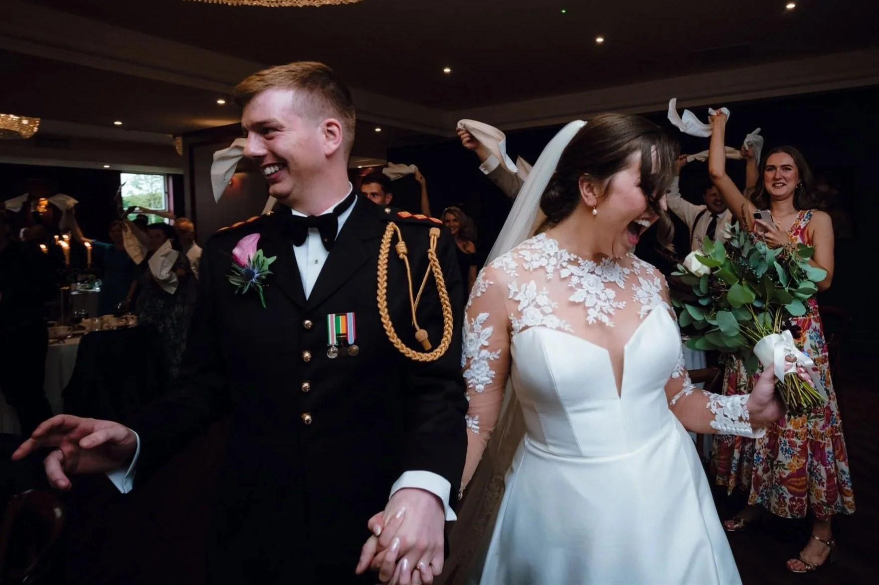 Bride and groom sharing a joyful moment during their wedding reception, with guests celebrating and tossing napkins in the background.