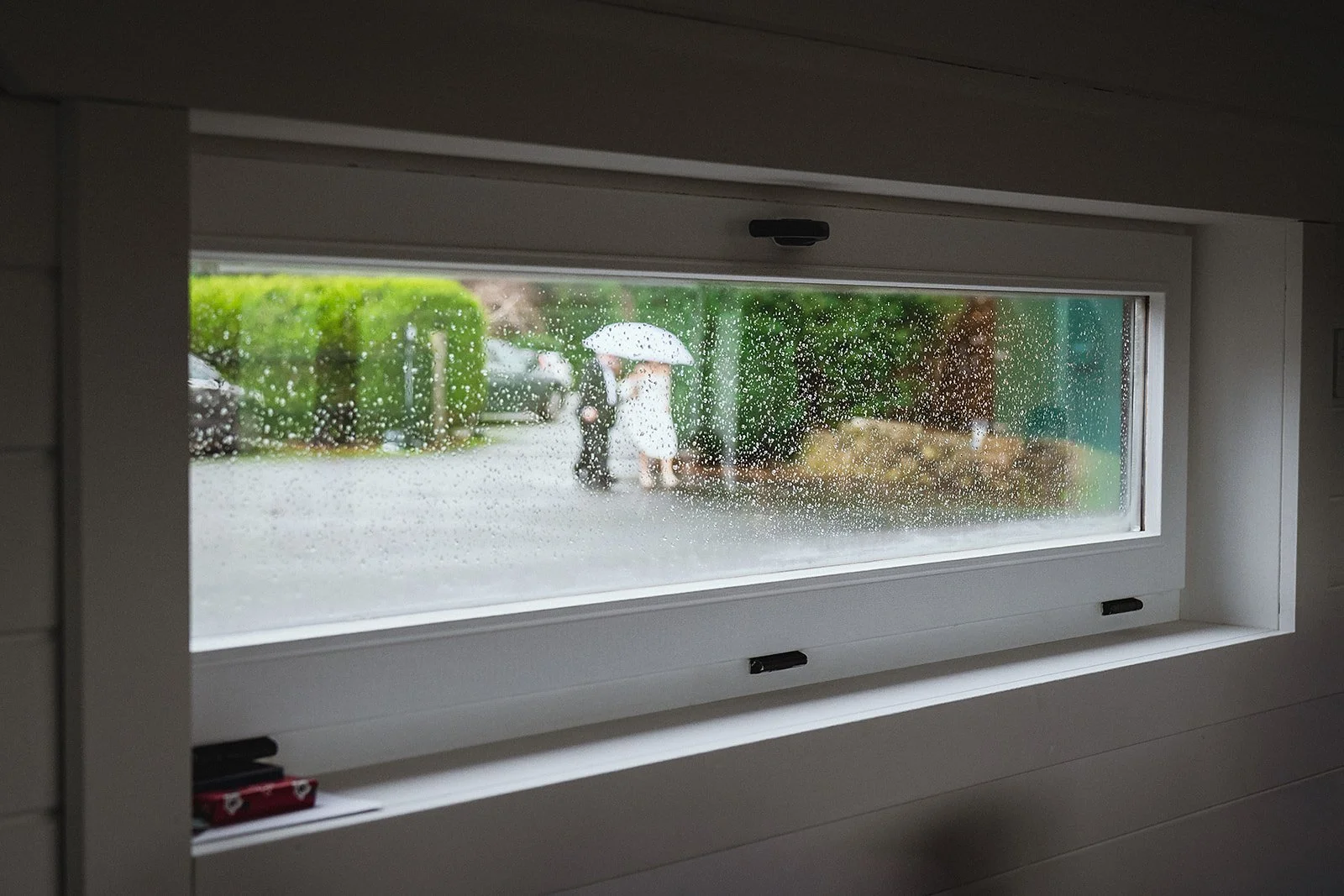 Rainy day viewed from a window with raindrops on the glass, showing people with umbrellas outside.