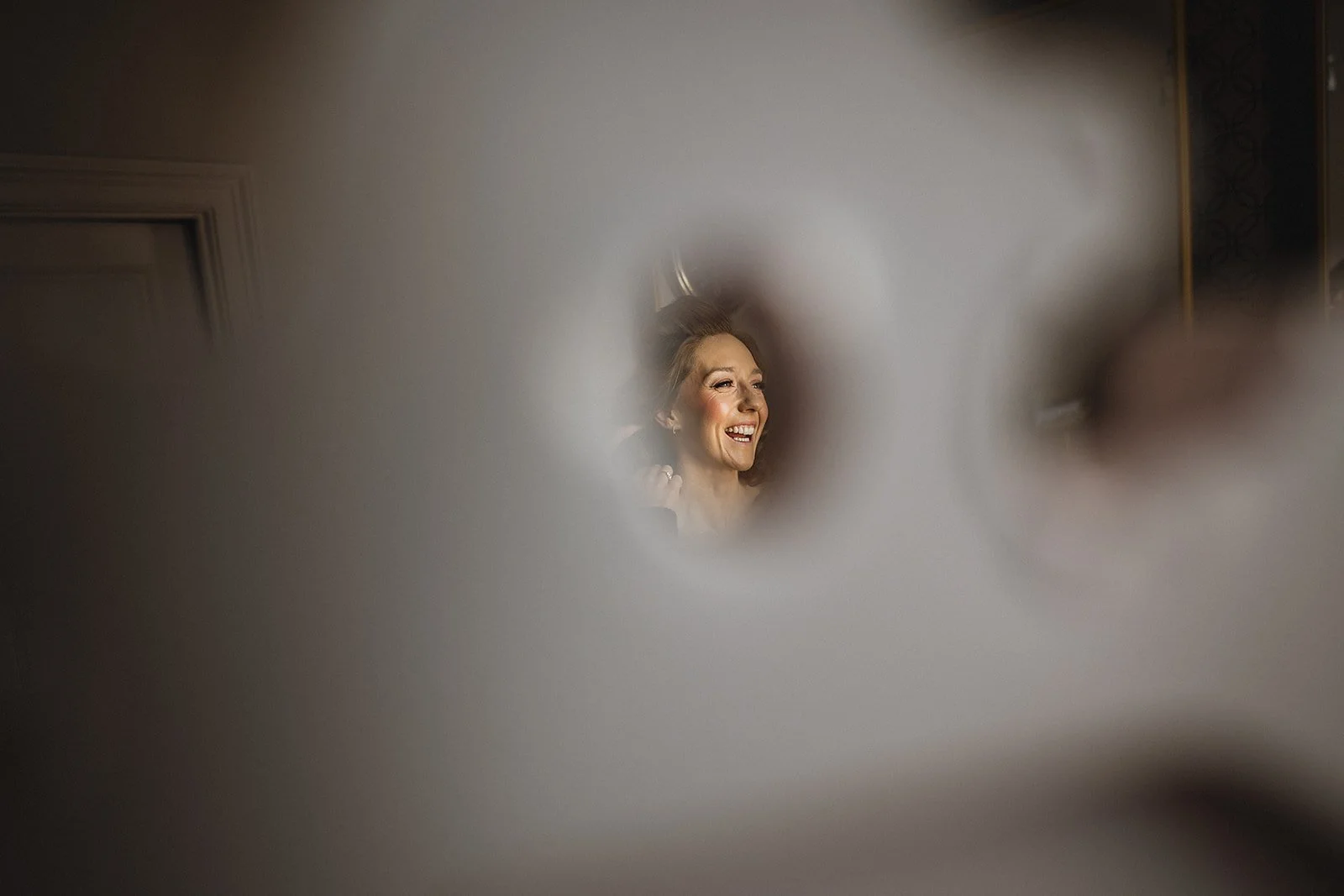A woman smiling and applying makeup in a mirror seen through a foggy glass or mirror.