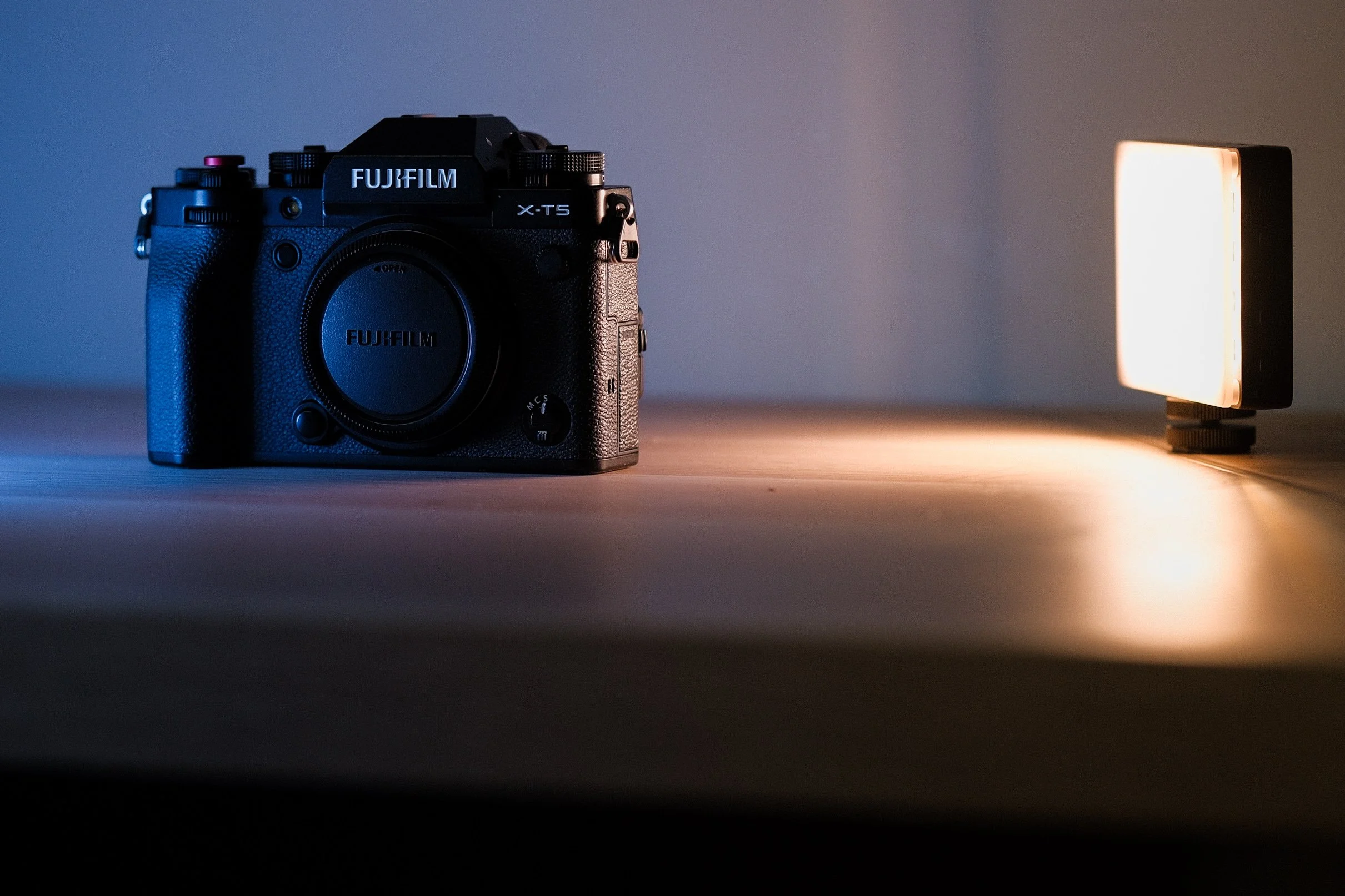 Fujifilm X-T5 camera on a wooden surface next to a small LED light.