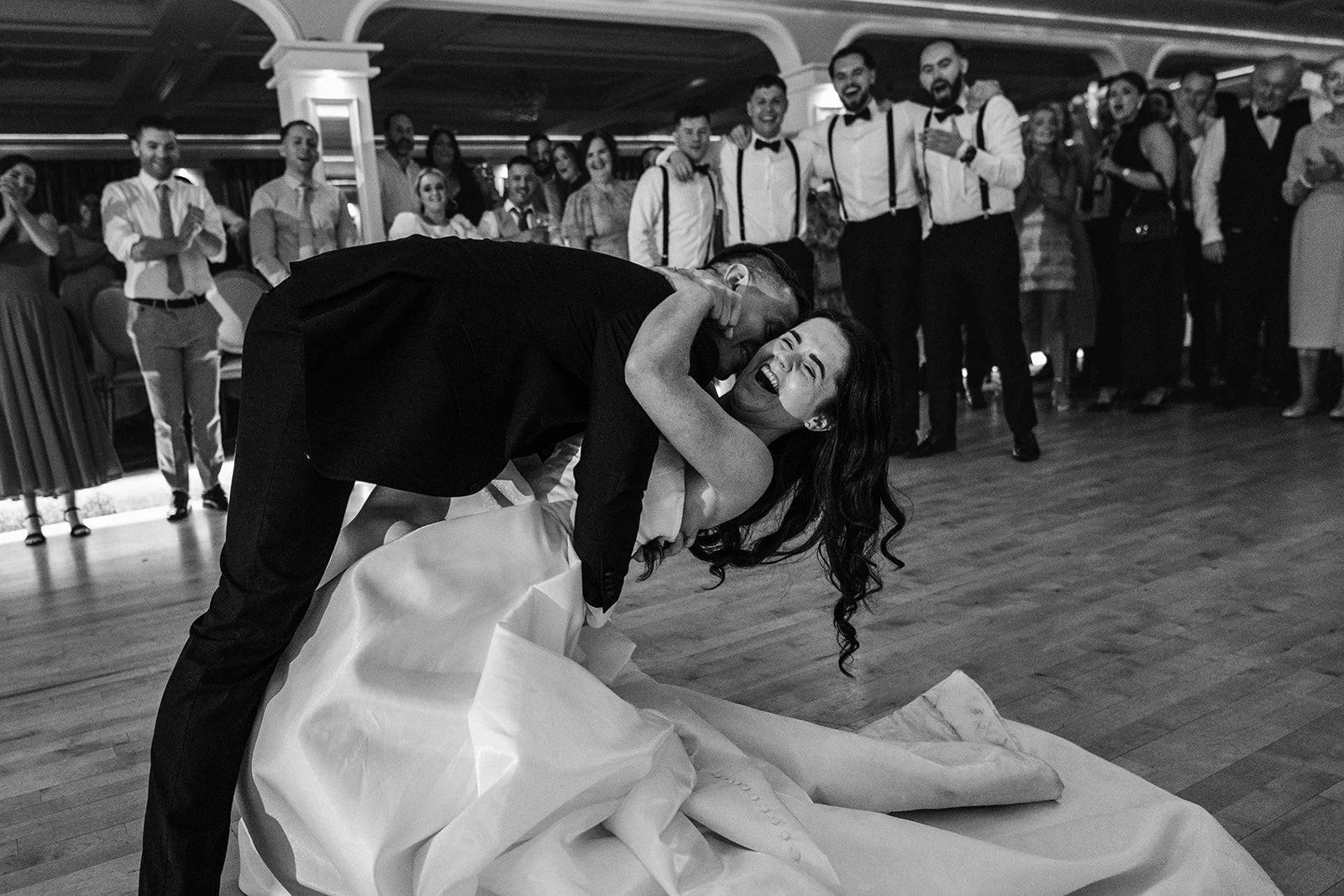 A bride and groom sharing a dance at their wedding reception with guests watching and smiling in the background.