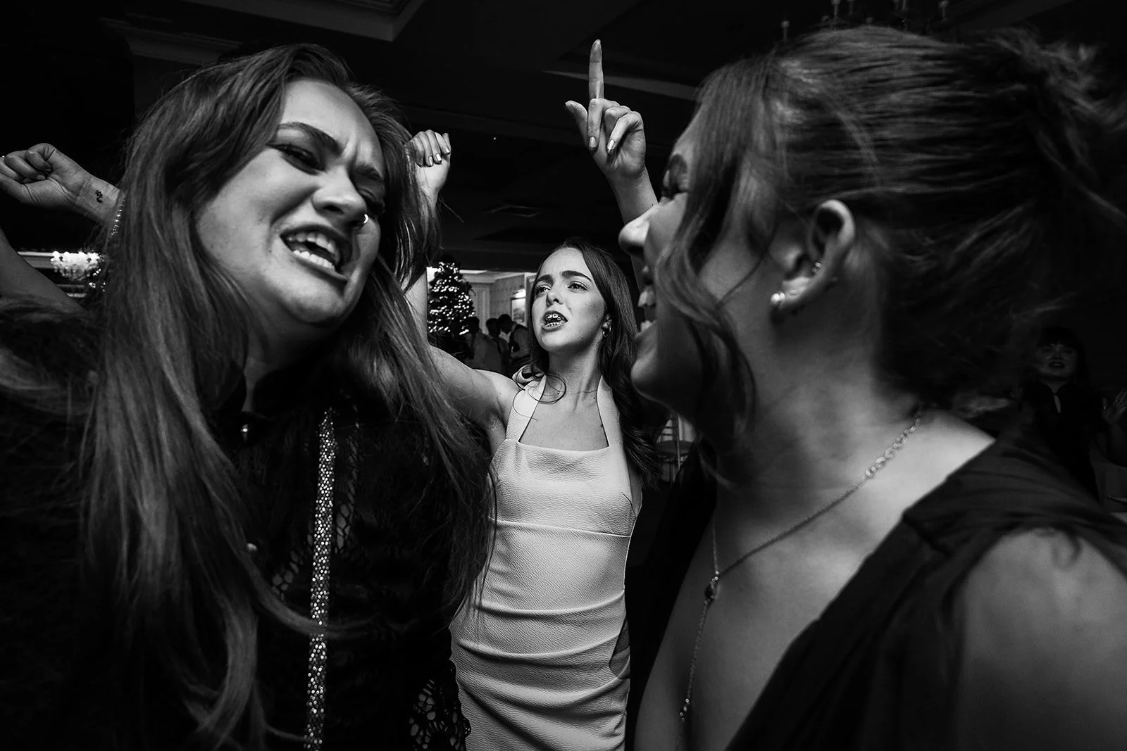 Three women with intense facial expressions engaged in a heated or passionate conversation at a party or event, black-and-white photo.