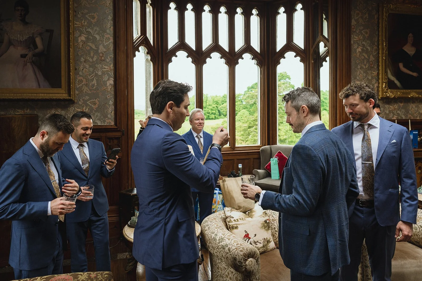 Group of men in suits having a meeting or discussion in a room with large stained glass windows and portraits on the wall.