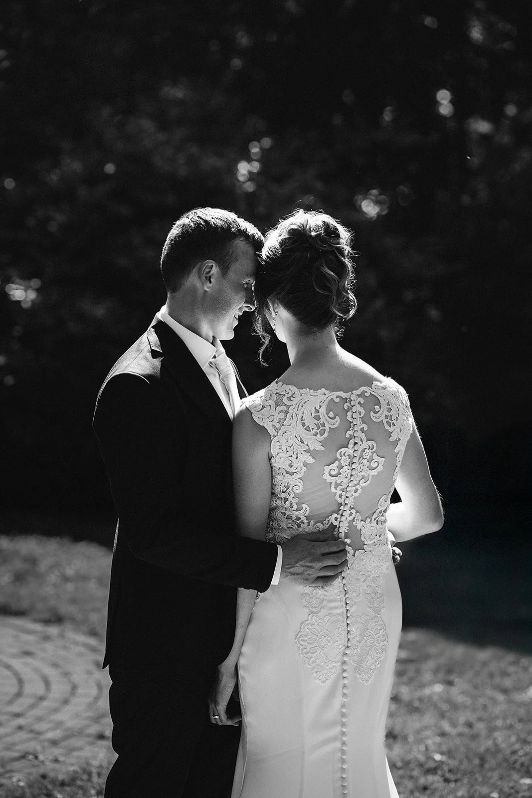 Black and white photo of a bride and groom sharing a moment outdoors, with the groom touching the bride's back.