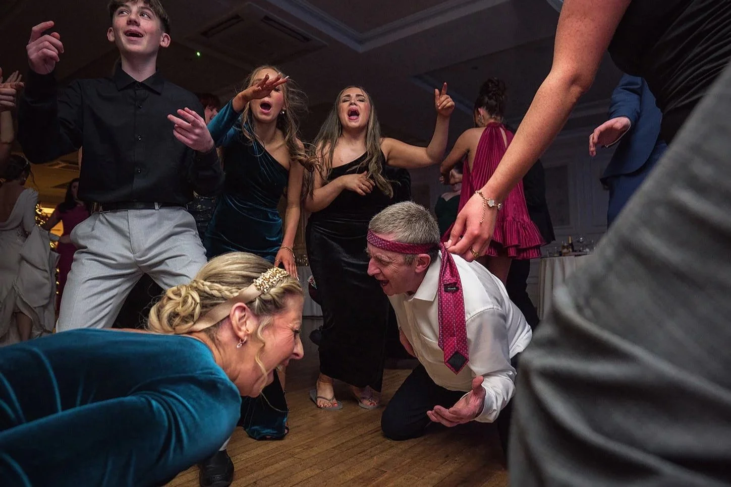 People dancing and celebrating at a lively party or wedding reception, with some individuals smiling, singing, and enjoying the moment.