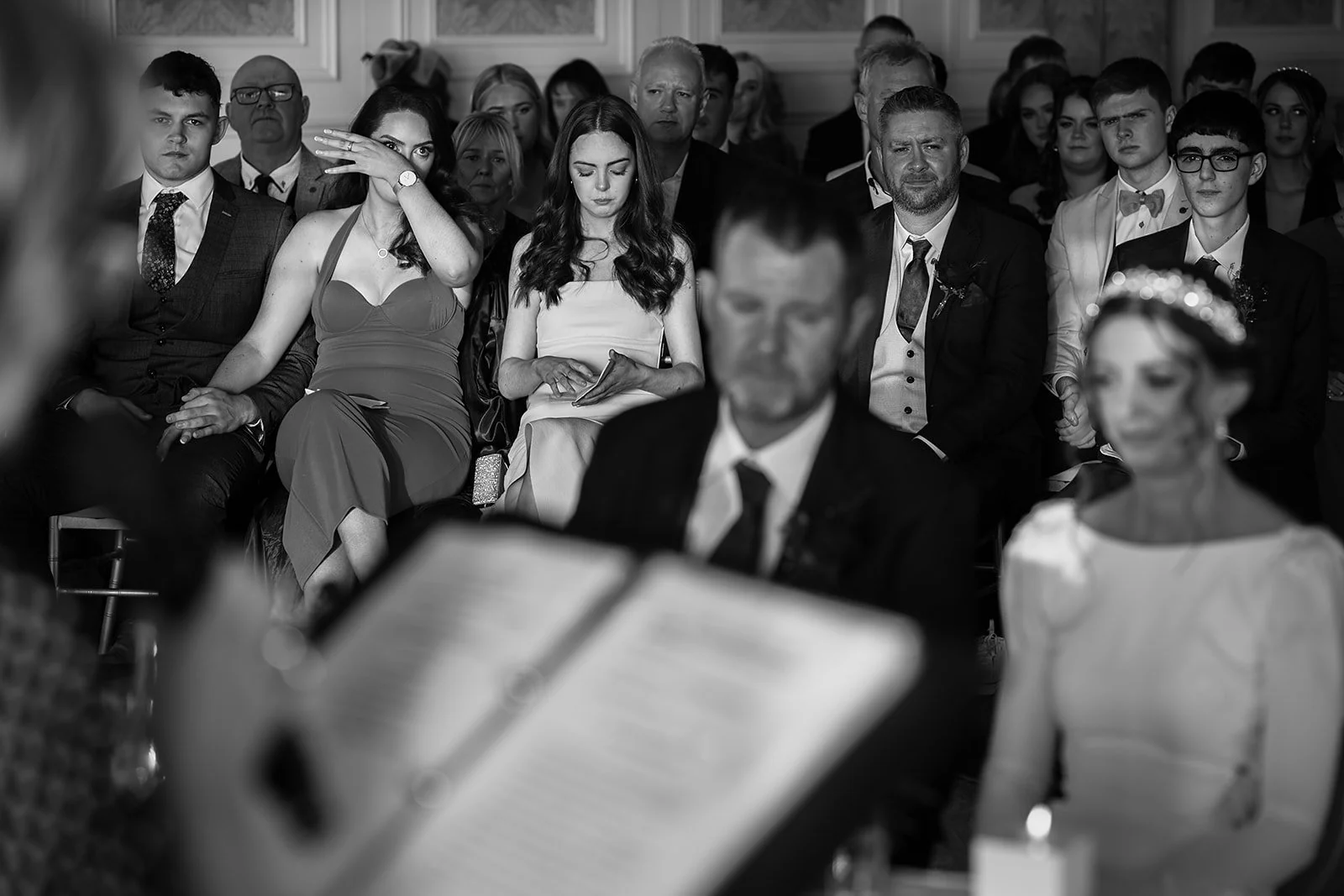 Black and white photo of people attending a formal event, sitting in rows and dressed in elegant attire, with a woman in a tiara visible in the foreground.