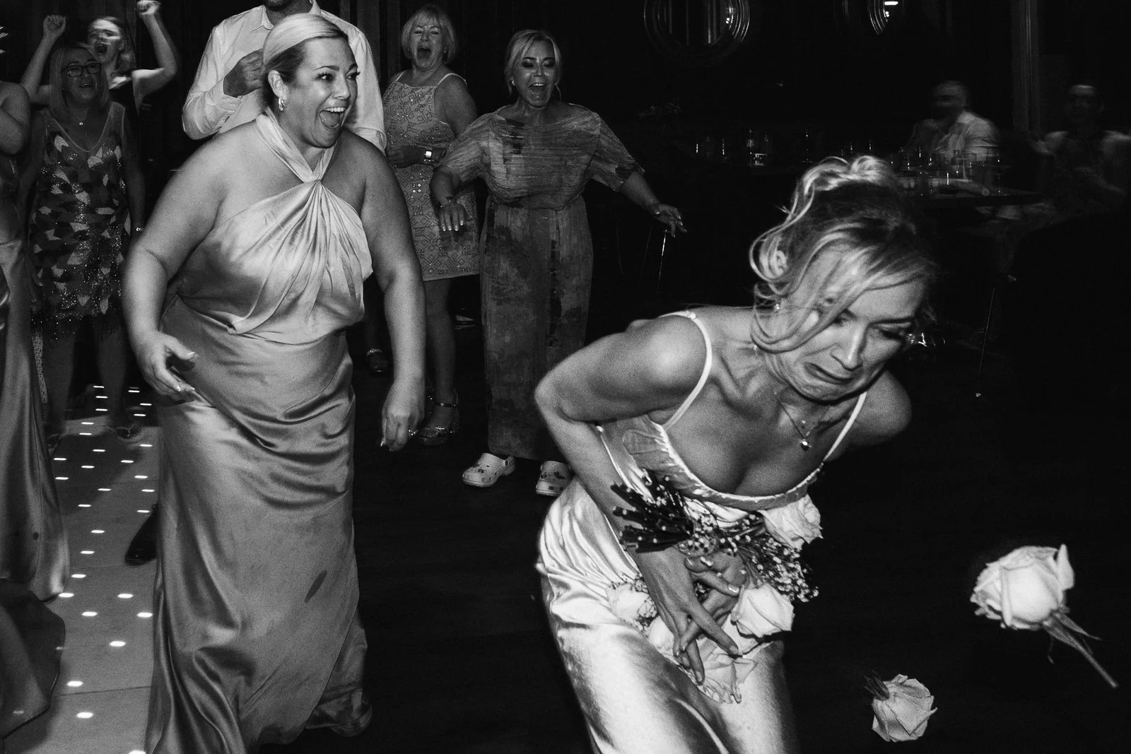 Women celebrating at a party, with one woman bending down clutching her stomach and others laughing and cheering in the background.