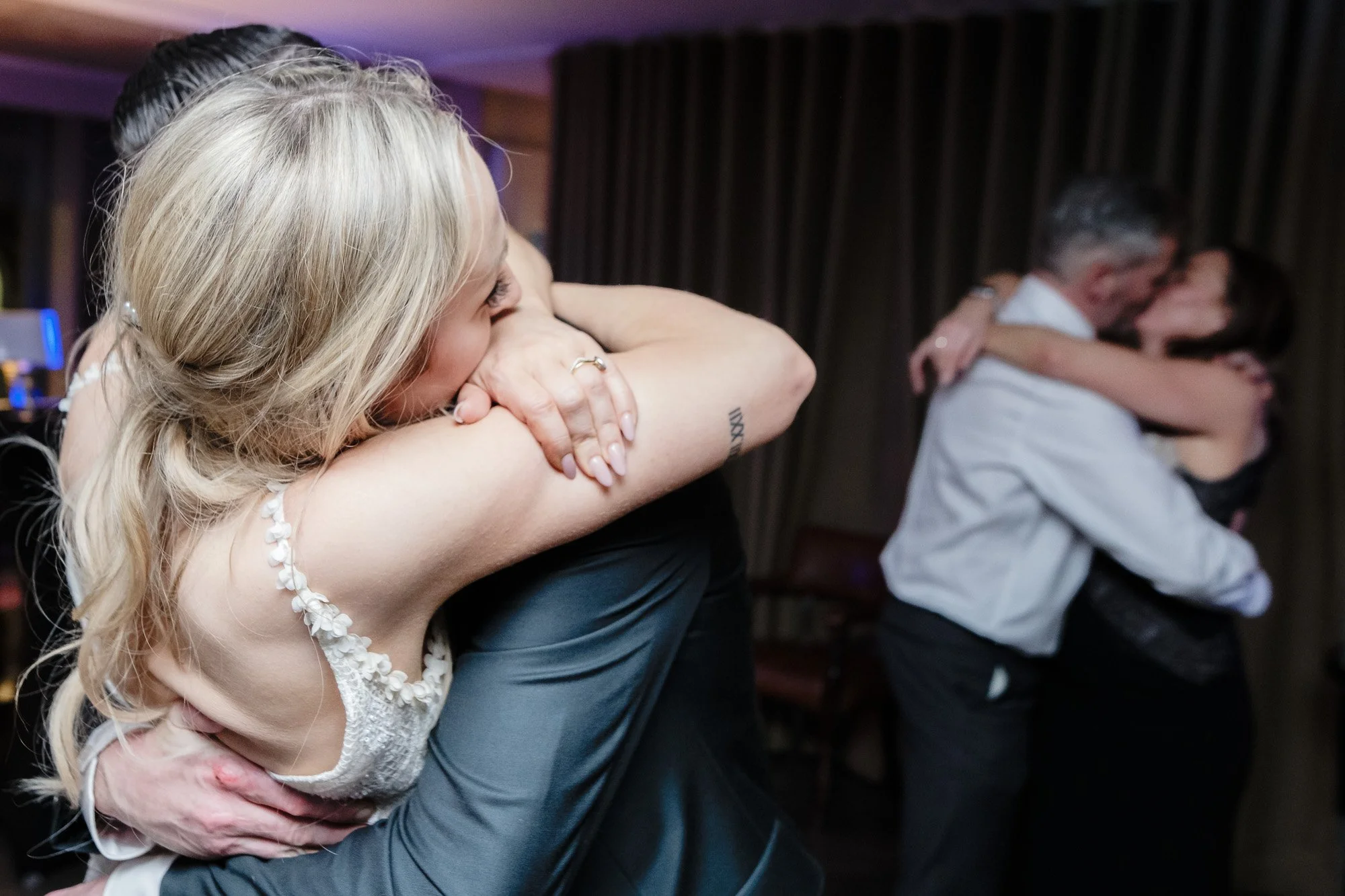 Three women embracing and hugging each other, appearing emotional during an event or celebration.