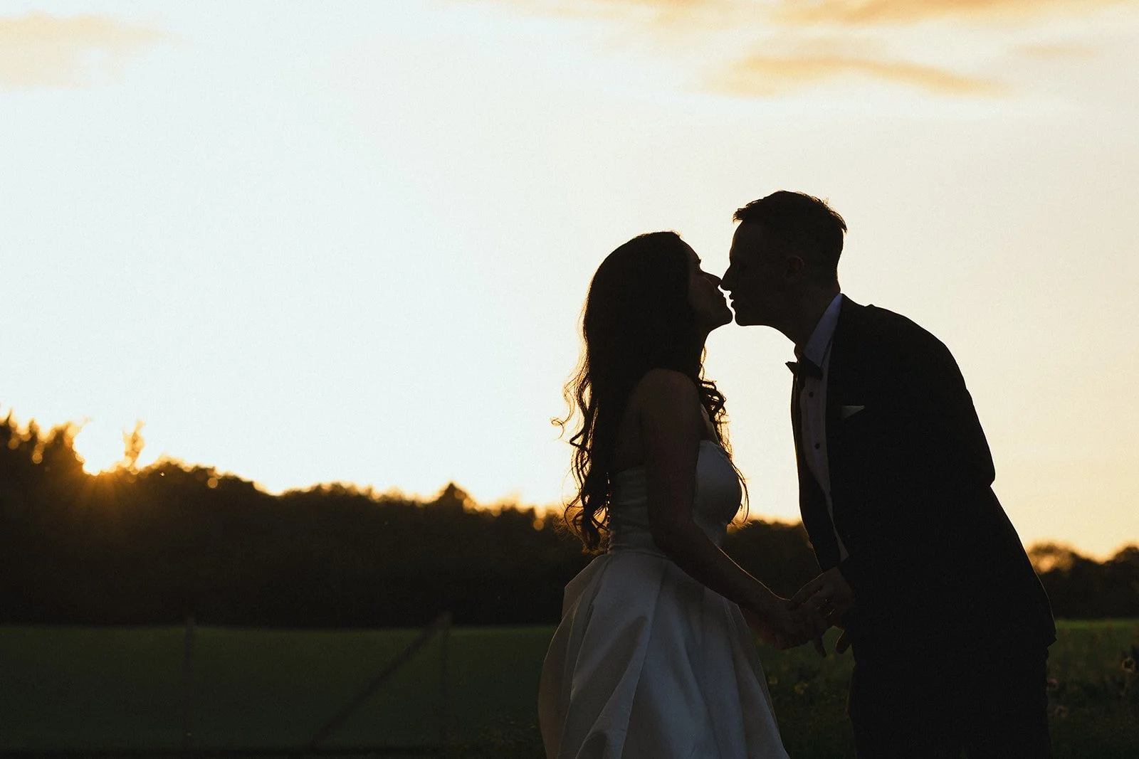 Silhouette of a couple kissing outdoors during sunset.