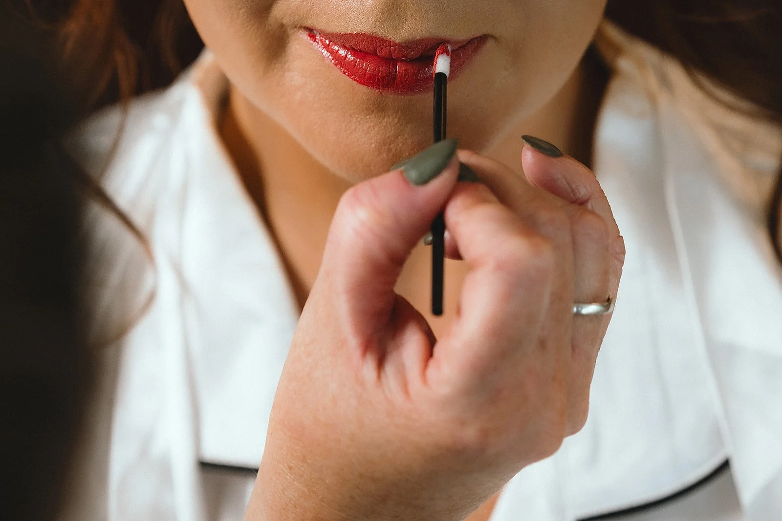 A woman applying red lipstick using a small applicator.