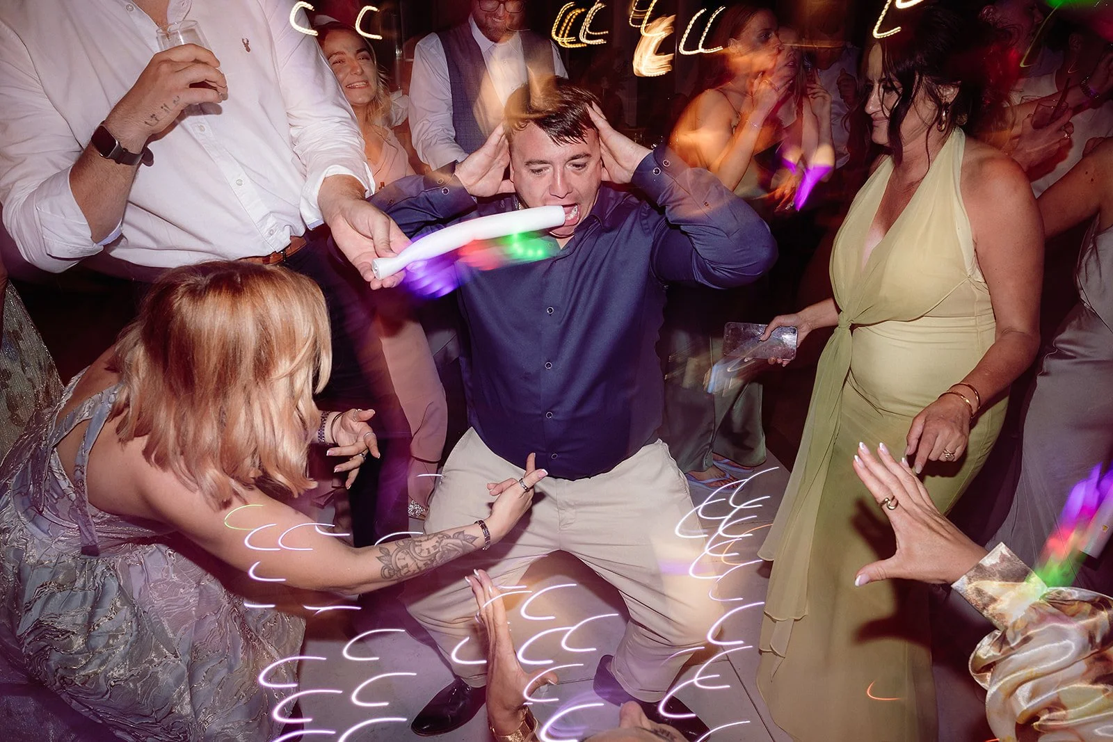 Person at a party dancing with colorful glow sticks, surrounded by other people also dancing and enjoying the celebration.