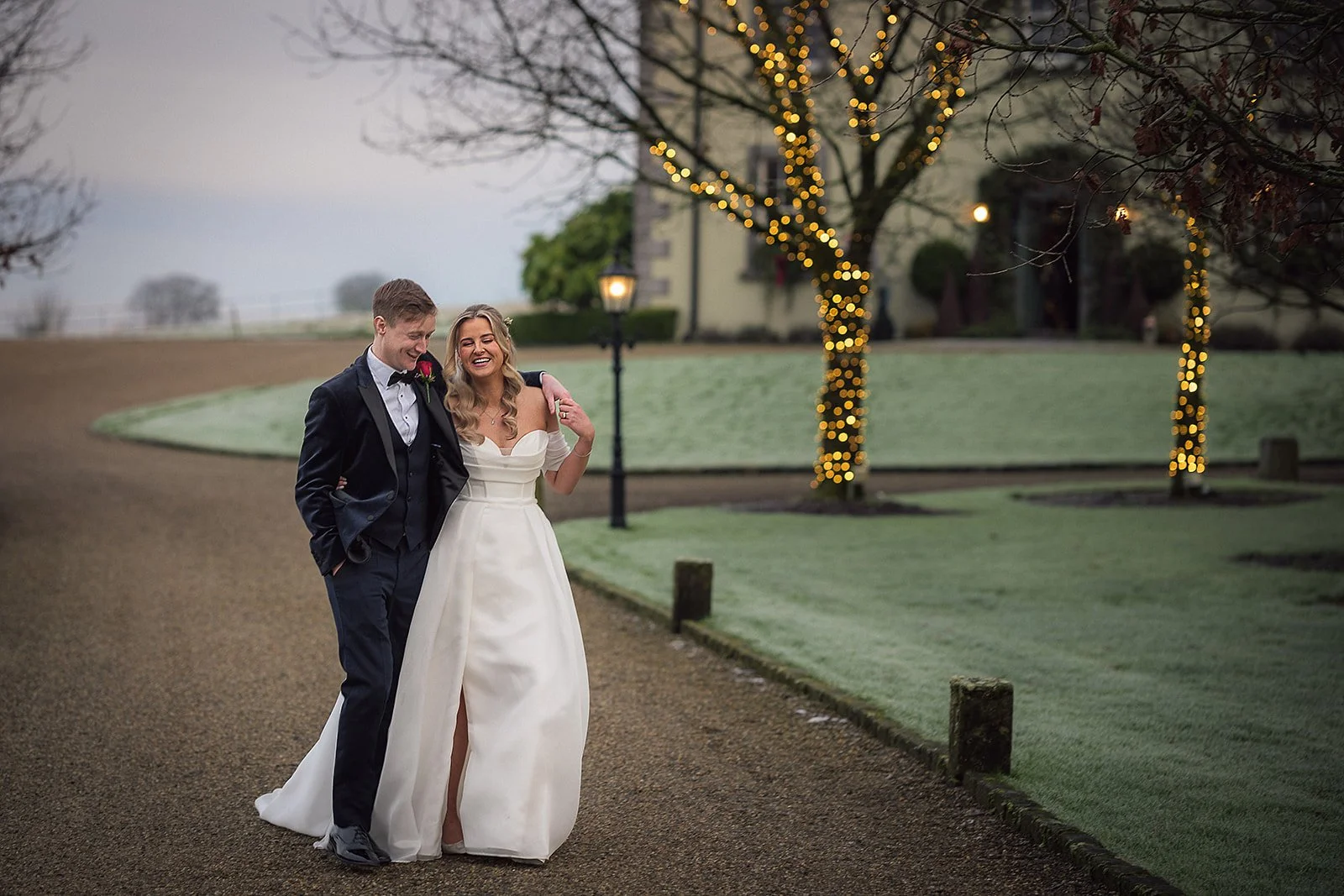 A bride and groom walking arm in arm outdoors during daytime.
