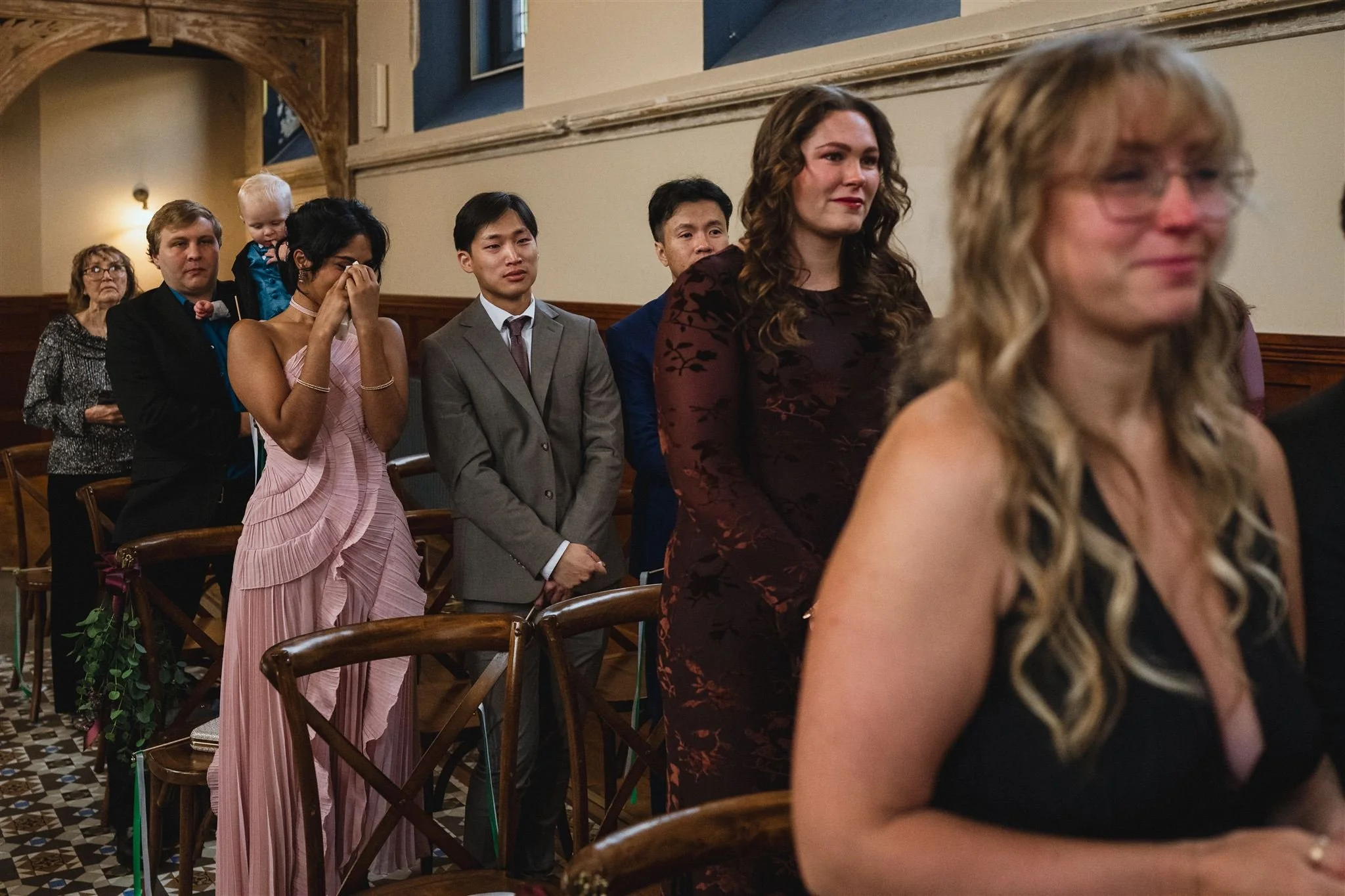 People attending a formal event in a church or banquet hall, standing in a line, some looking emotional, some crying, others looking serious or composed.