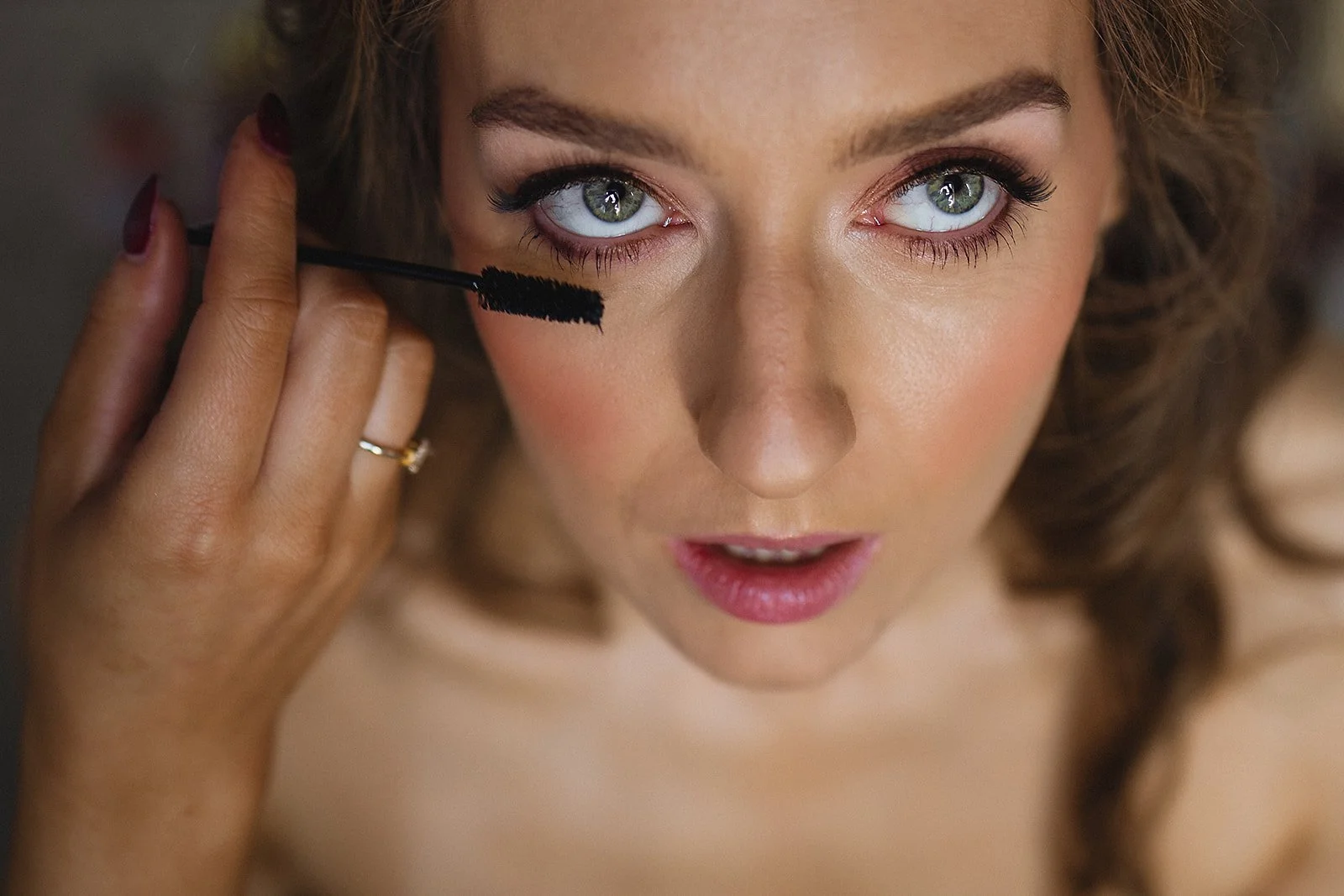 Close-up of a woman applying mascara to her eyelashes, looking into a mirror.
