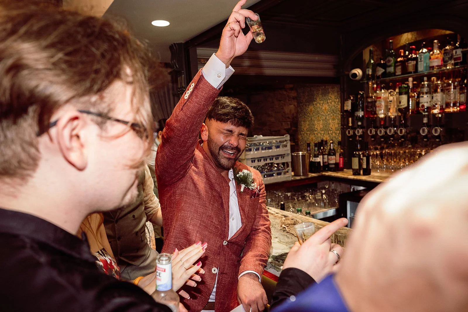 Man in a red suit celebrating with a drink at a bar.