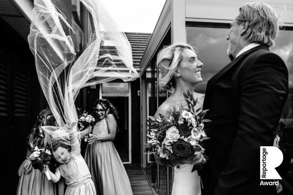 A bride and groom smile at each other on a balcony, with bridesmaids and flower girls nearby.