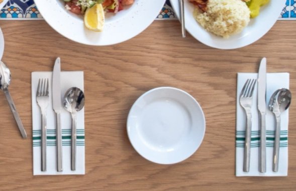 Empty white plate on a wooden table with neatly arranged fork, knife, and spoon on napkins on either side.