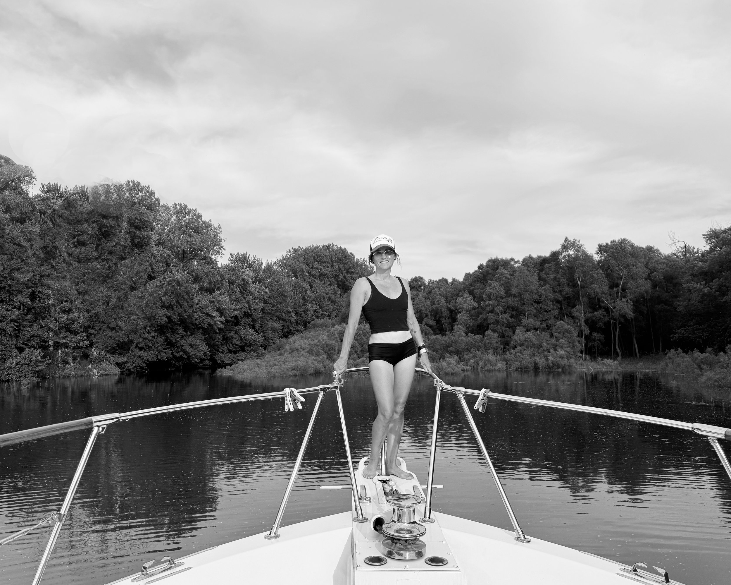 Black and white photo of a massage table in a room with hardwood floors and minimal furniture, including a small shelving unit and a framed picture on the wall.
