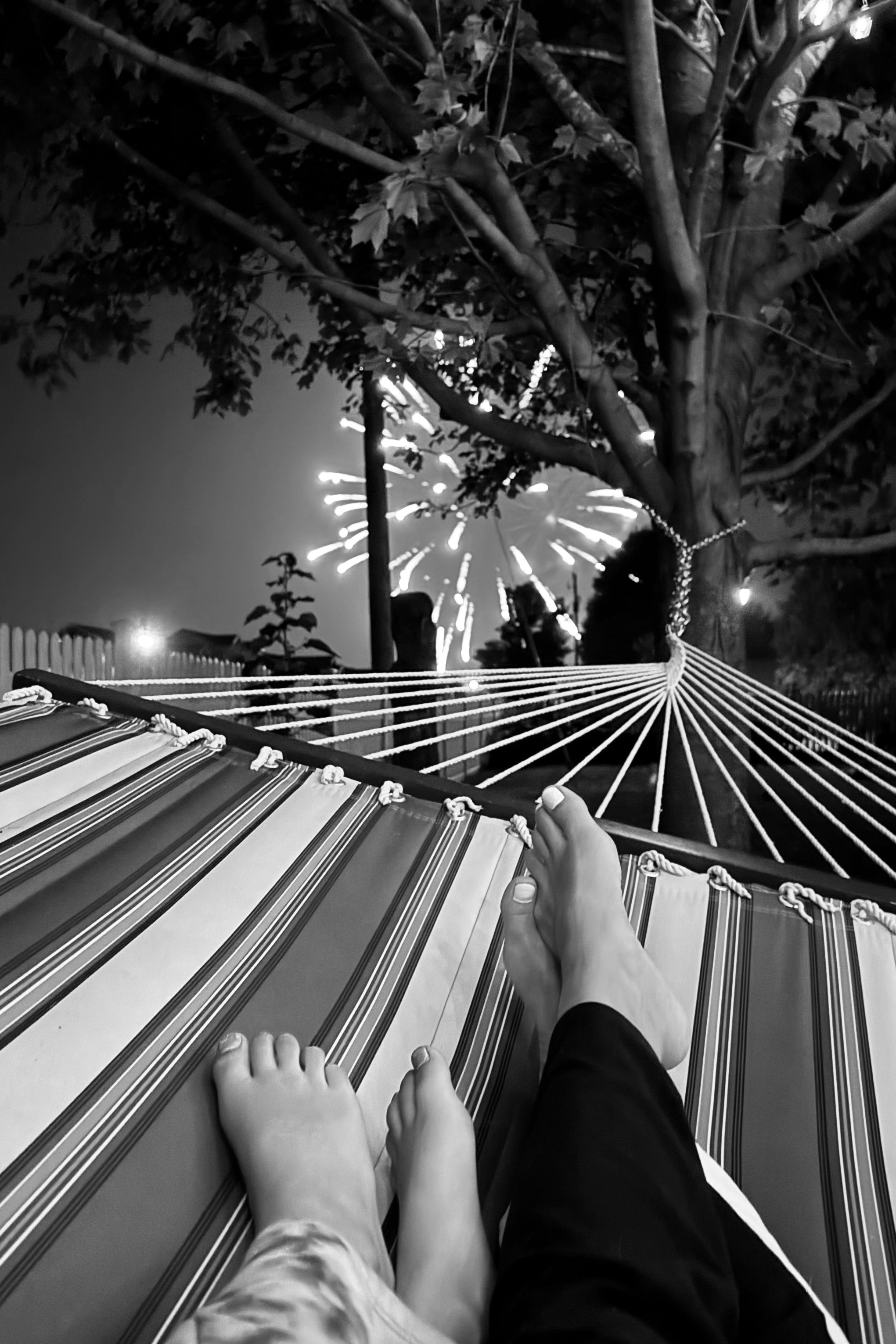 A black and white photo of an elderly couple walking together in a park, holding hands, with trees and a dirt path around them.