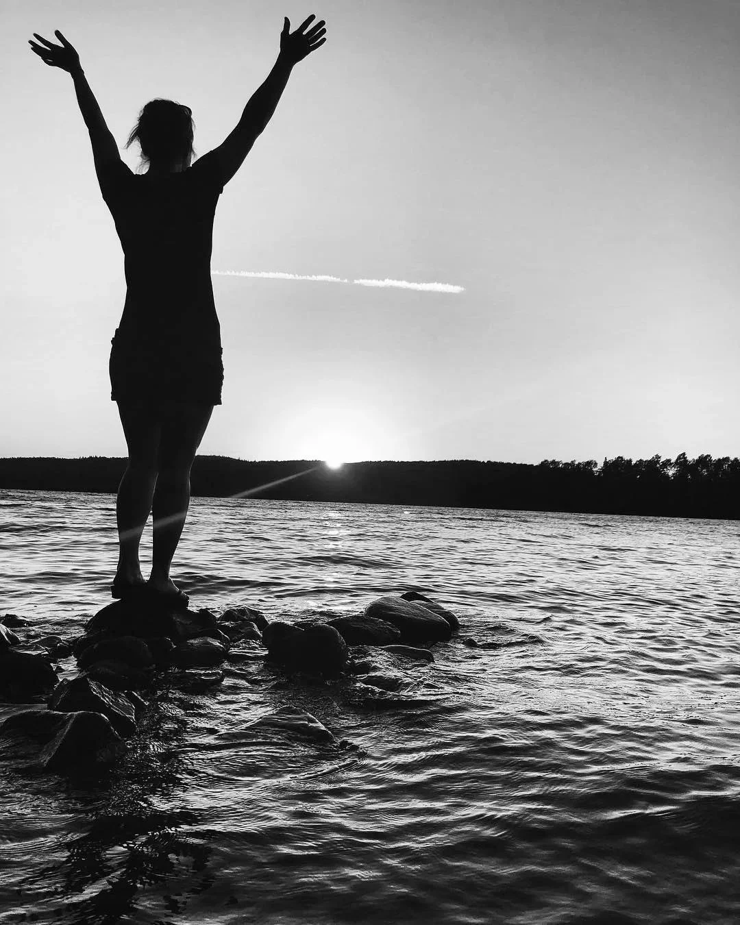 Black and white photo of a massage table in a room with hardwood floors and minimal furniture, including a small shelving unit and a framed picture on the wall.