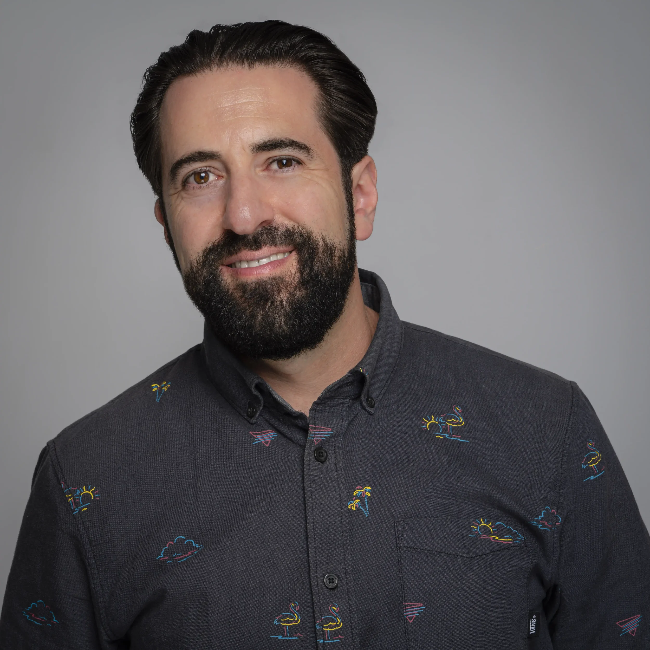 Dan Levy, a man with dark hair and a beard wearing a charcoal shirt and smiling.