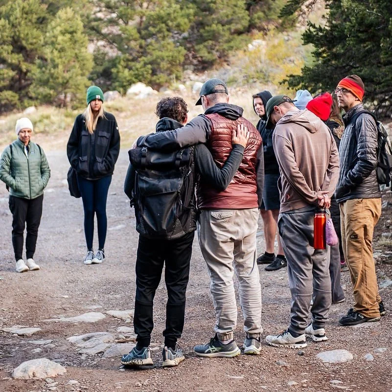 Two male retreat guests and a group of participants in a mindful breathing circle during a transformational retreat in nature.