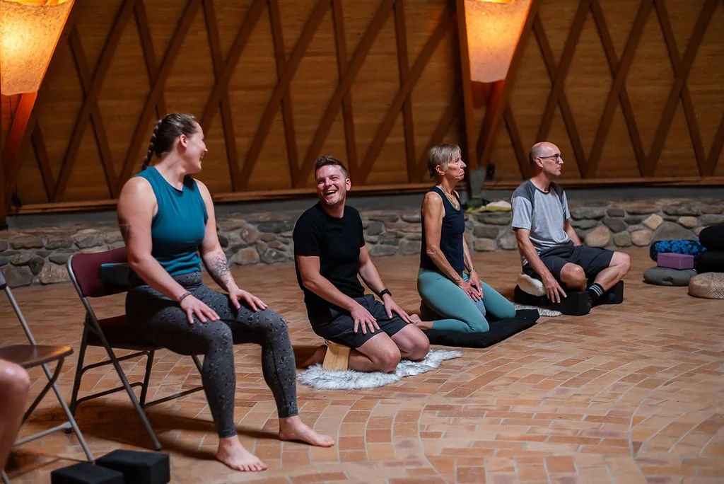 Retreat guests laughing with one another while another sits preparing for meditation.