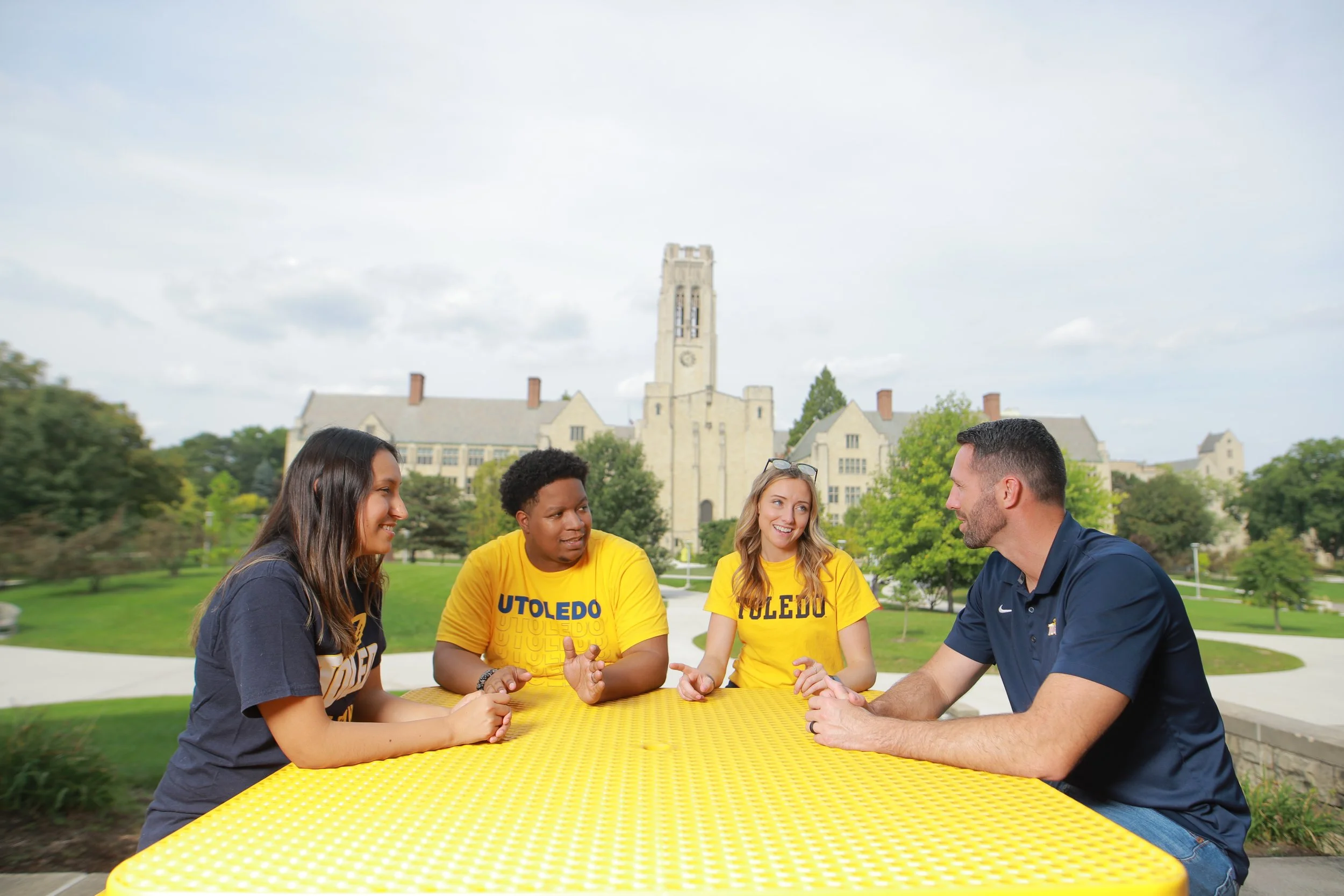 Four young alumni sitting at a picnic table talking