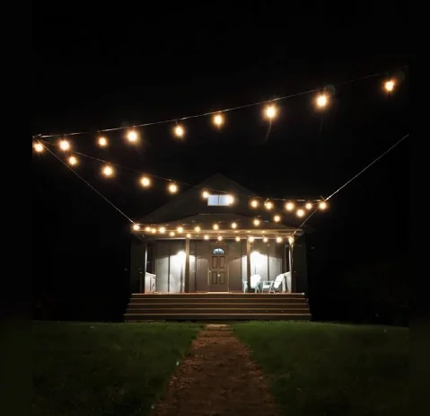 Boutique hotel exterior at night in the Catskills illuminated with hanging string lights and a glowing front porch.