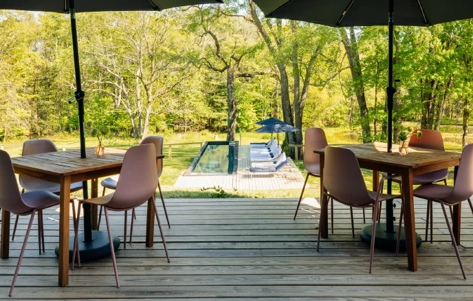 Outdoor patio dining area overlooking a heated pool and wooded landscape at a Catskills retreat.
