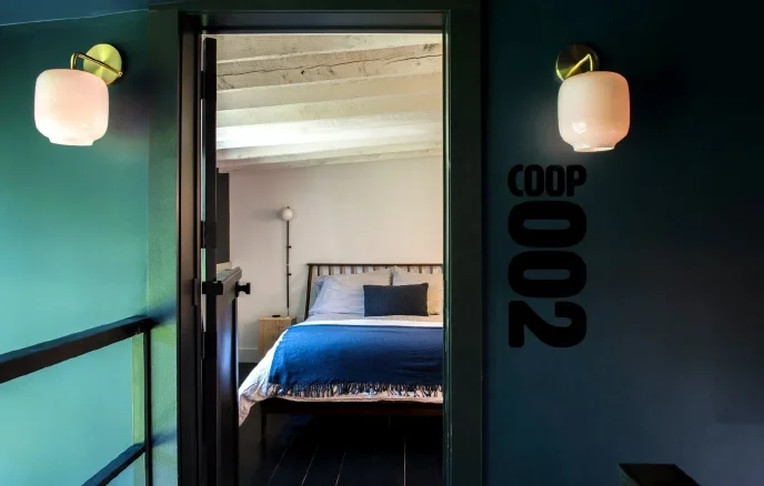 Cozy boutique hotel bedroom labeled Coop 002 with modern decor and soft lighting in the Catskills.