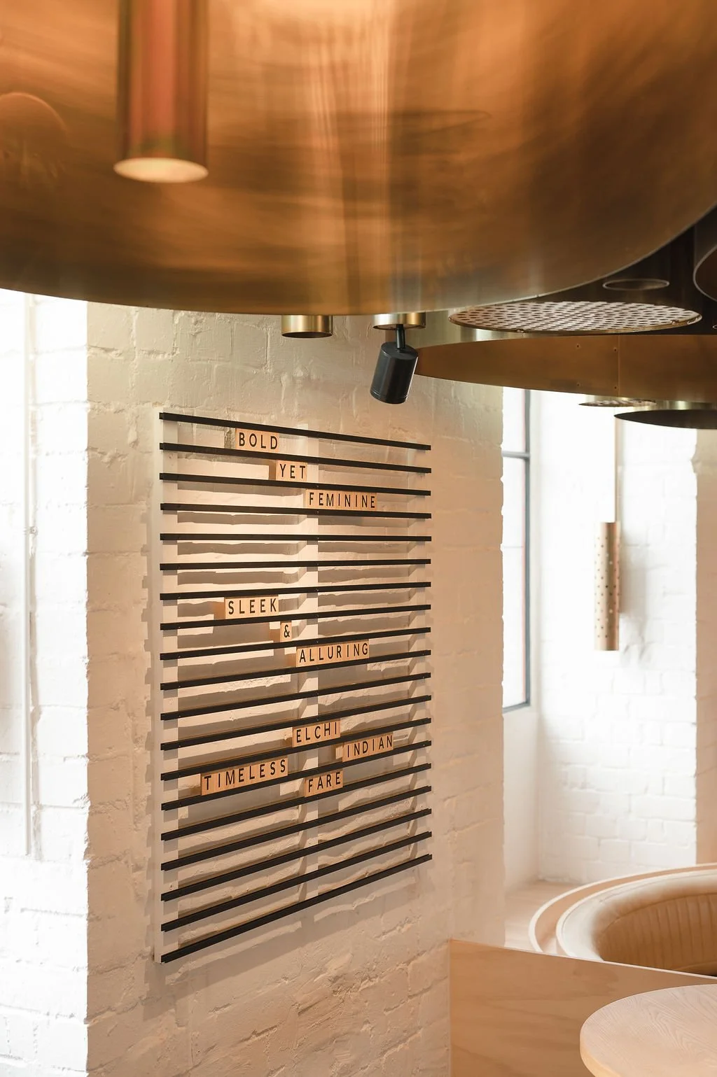 Slatted lettering wall installation beneath brass light fittings at Elchi