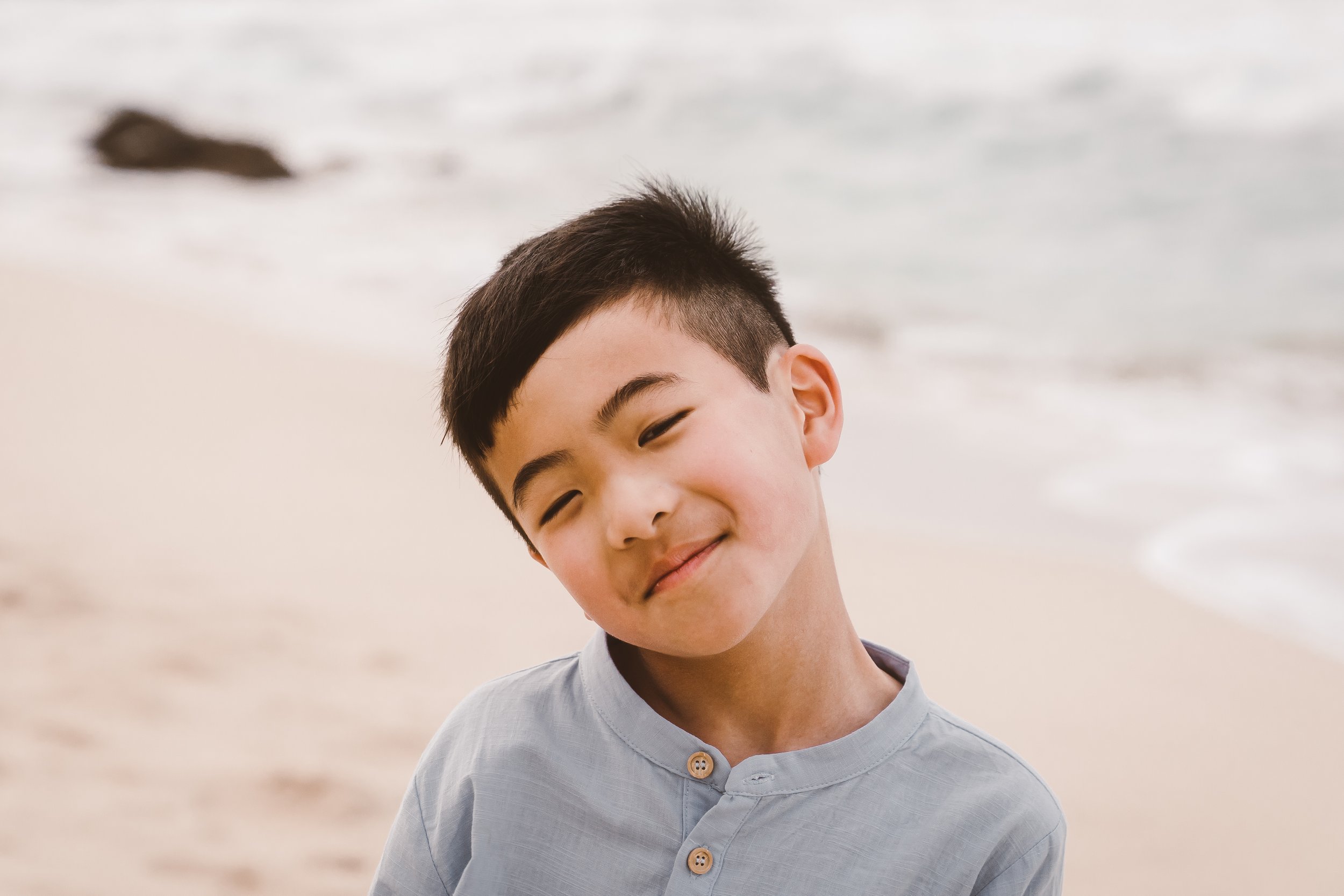 Young boy makes silly face for portraits on beach at sunset Maui HI