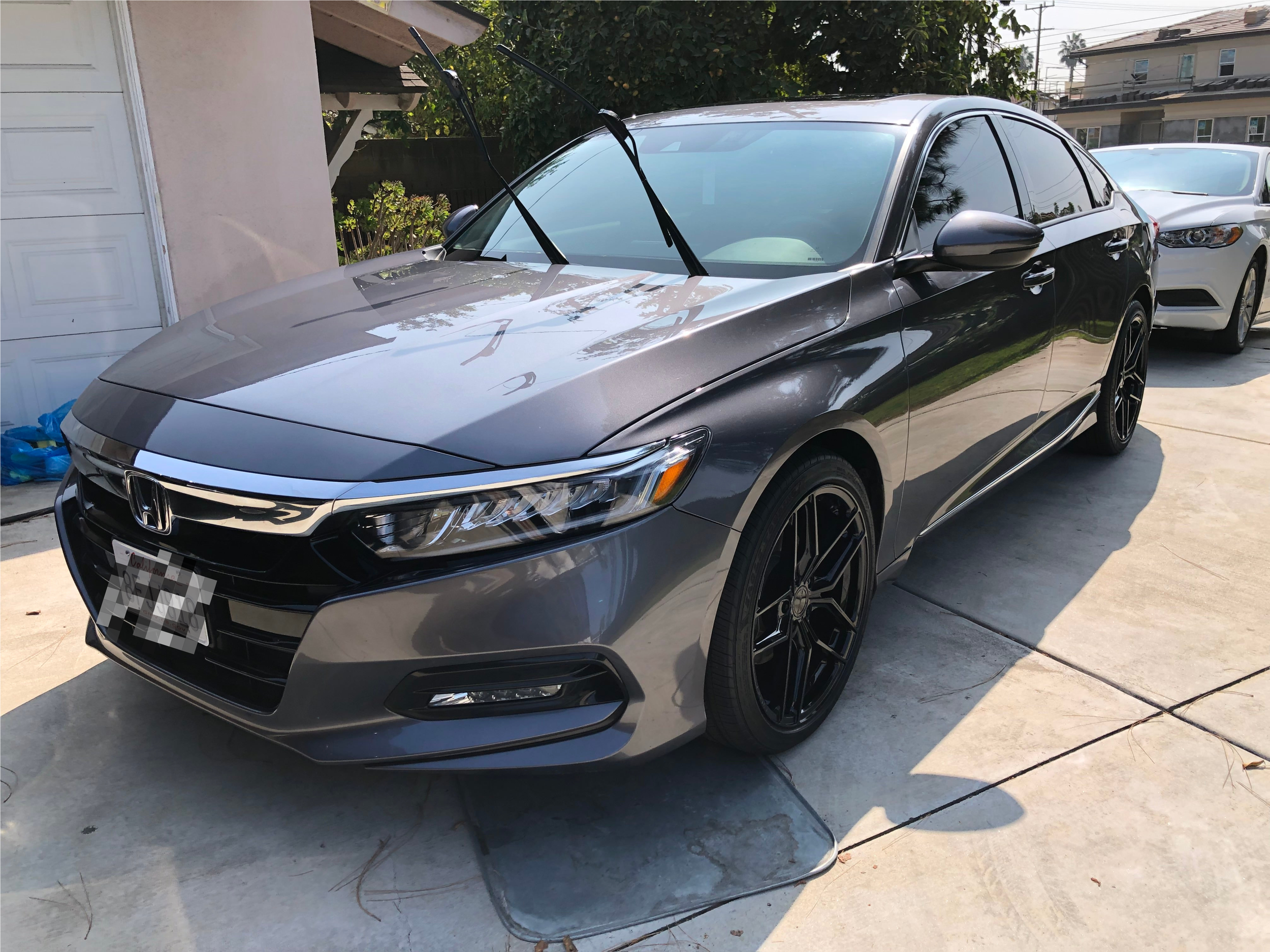 Gray Honda sedan parked in a driveway, with windshield wipers raised, beside a white car and a garage.