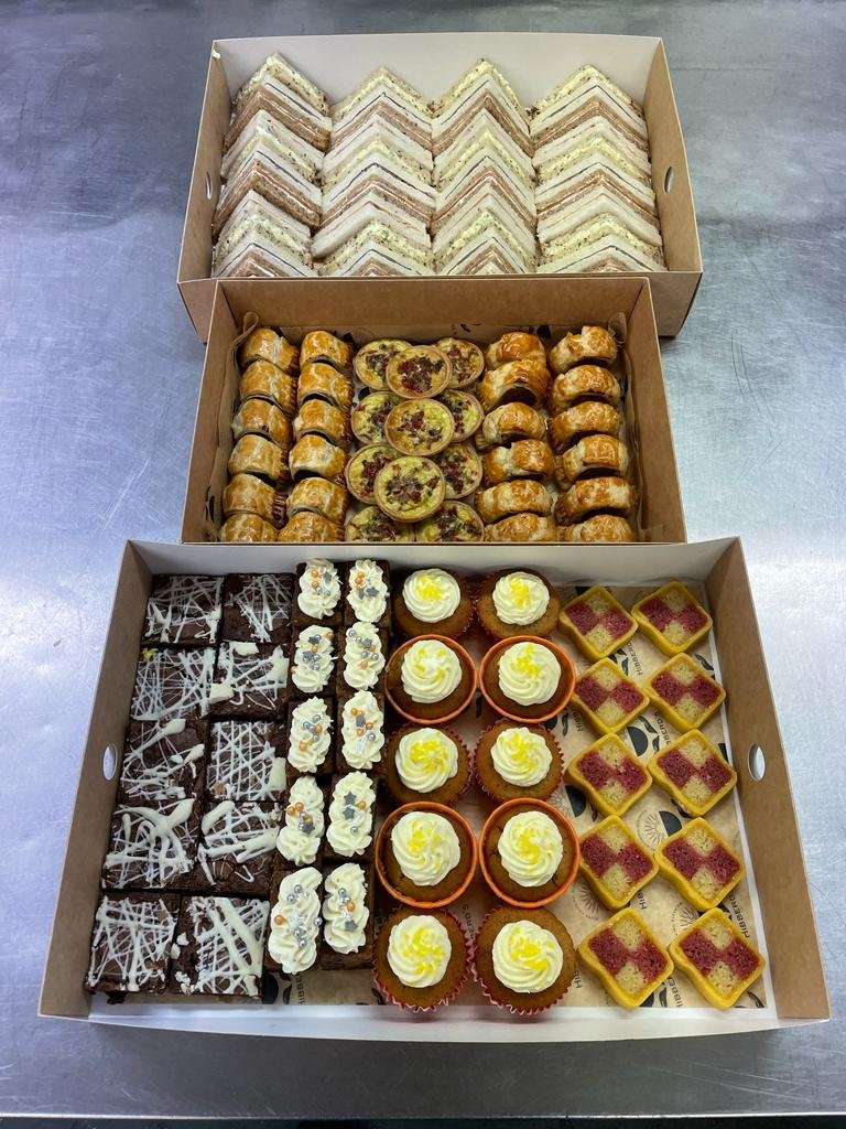 A selection of boxes containing afternoon tea items such as brownie bites, sandwiches and sausage rolls