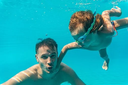 Dad and son are having fun underwater in resort swimming pool